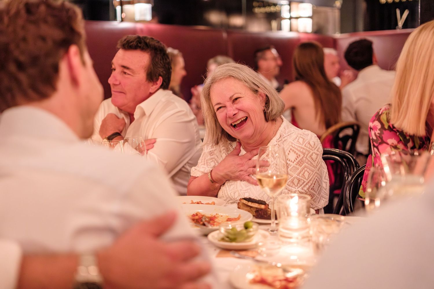 Wedding guests laugh joyfully during an evening reception with candlelit tables.