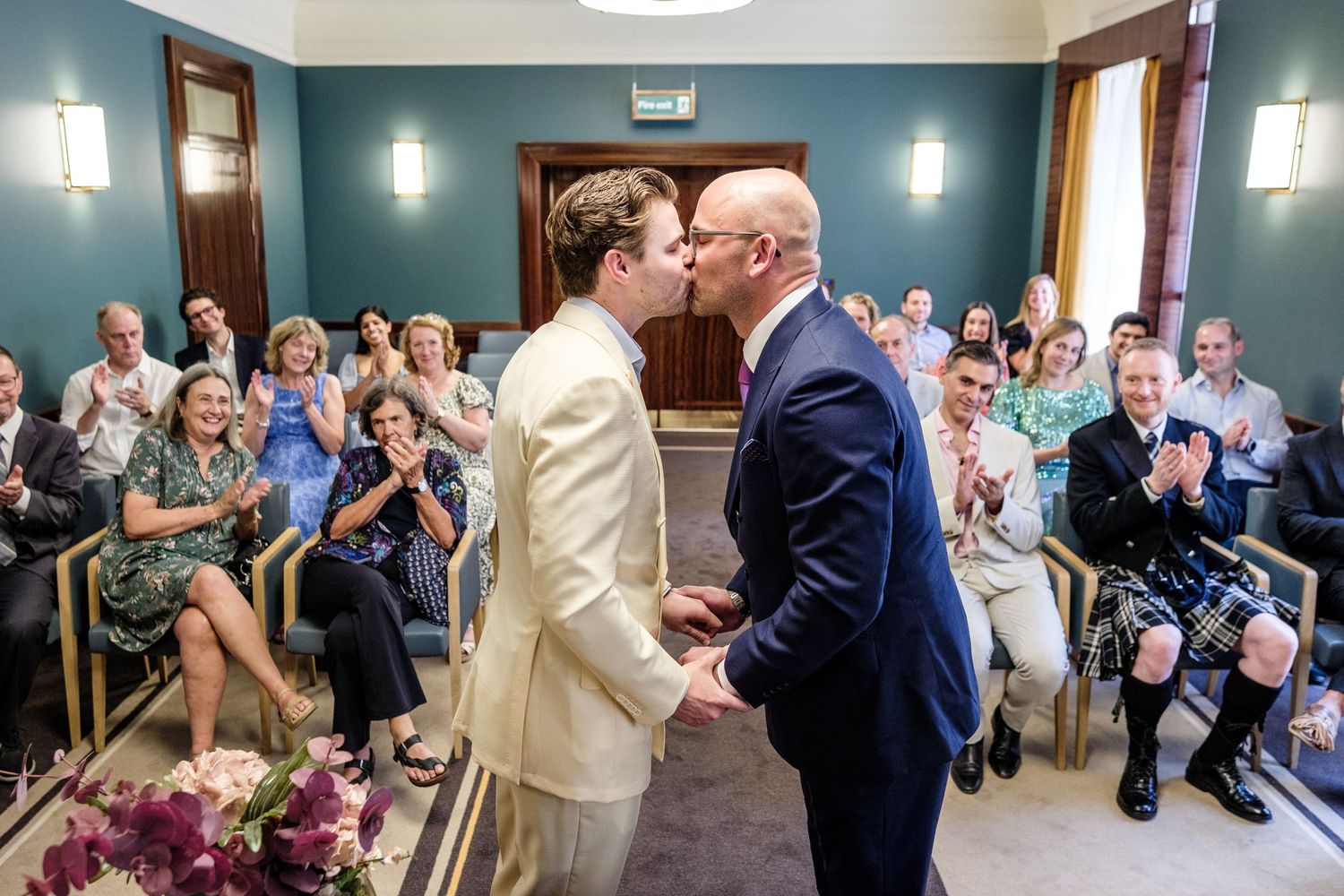 A panoramic wedding ceremony sequence shows tender moments and loving embraces while guests watch in a blue-walled room.