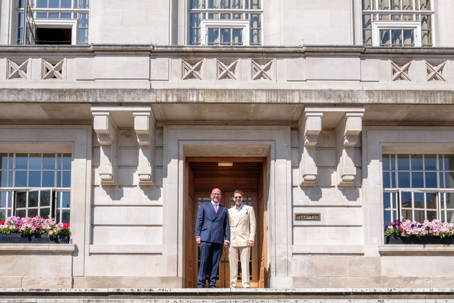 A couple standing in a grand doorway of a historic stone building with ornate architectural details and flower boxes.