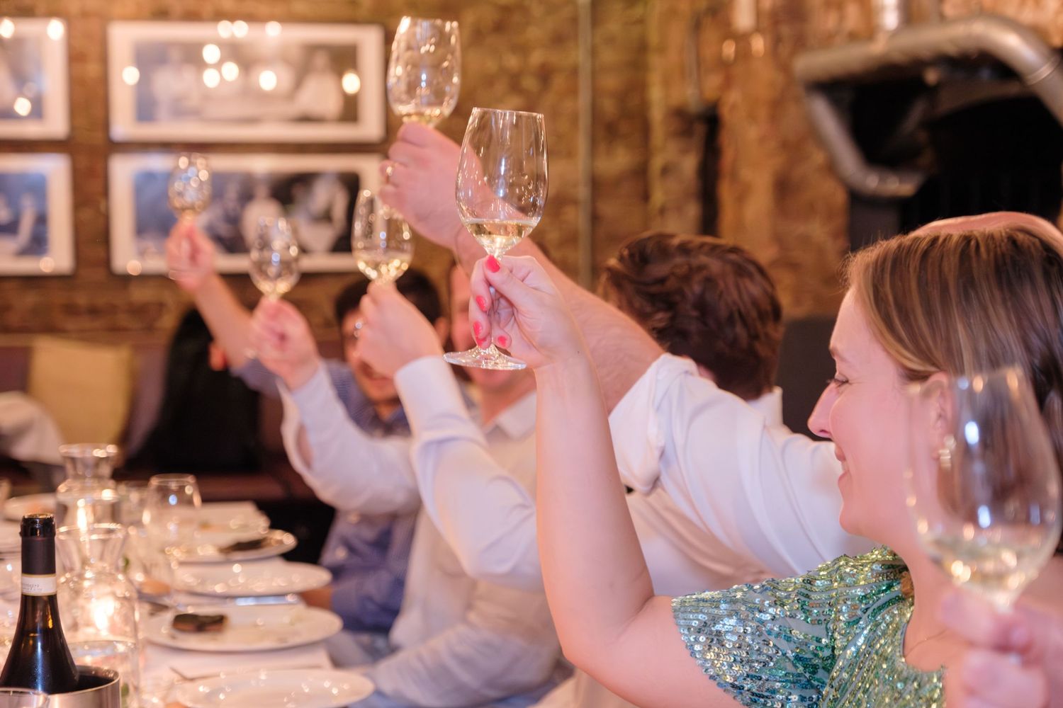 Guests raise wine glasses in a celebratory toast during a festive dinner party in a restaurant with exposed brick walls.