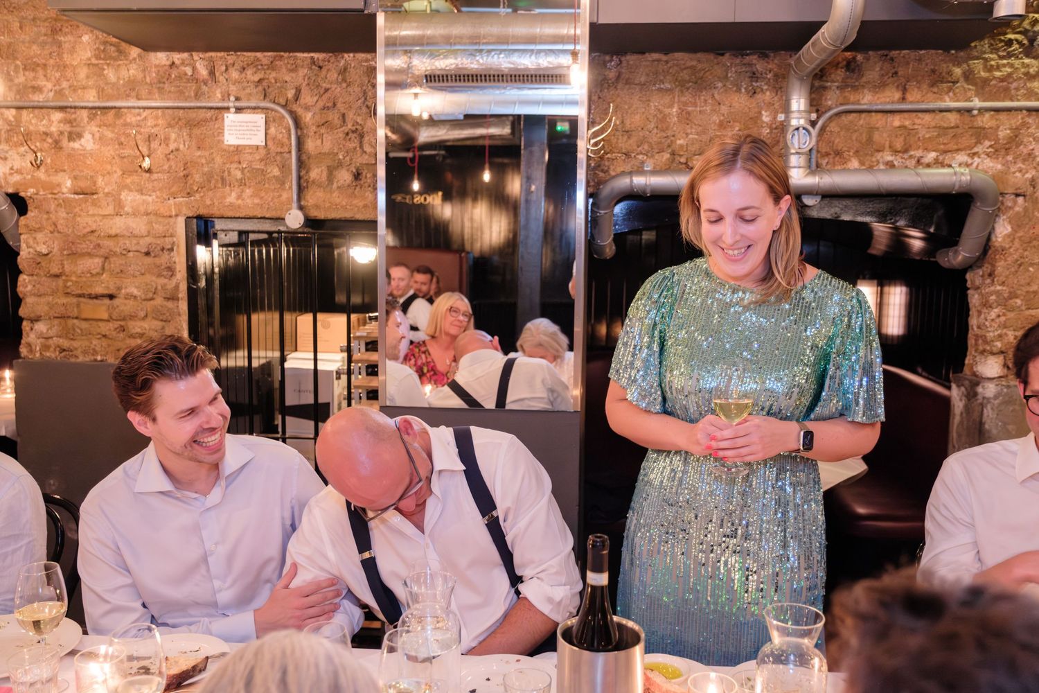A group gathered in a rustic brick-walled restaurant space laugh and smile during a social gathering over drinks.