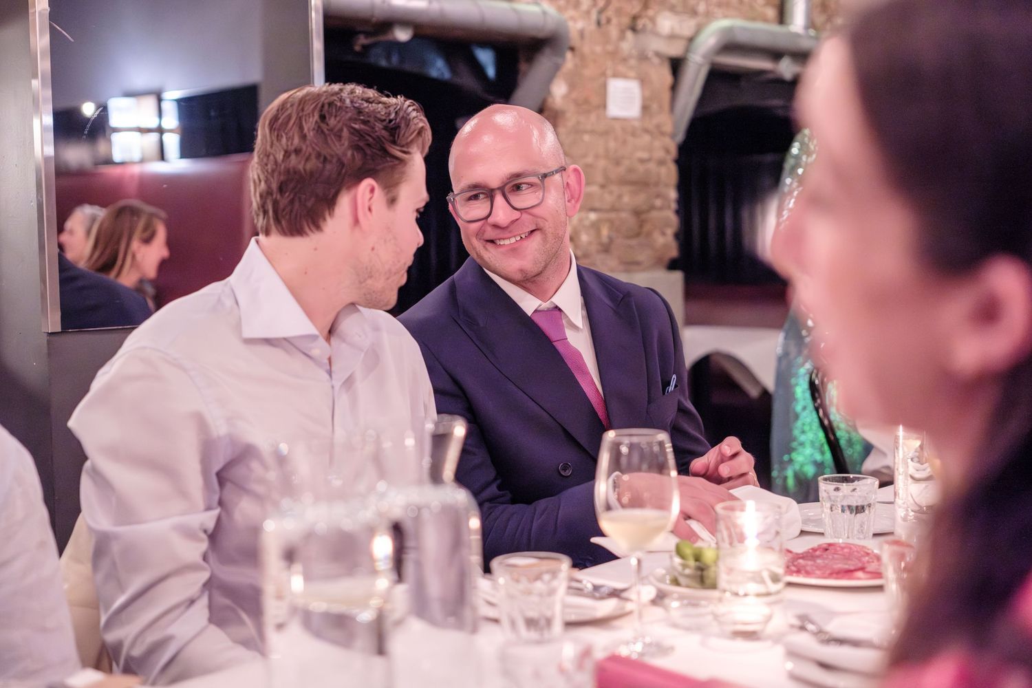 People engaged in conversation around a dining table at an elegant restaurant gathering.