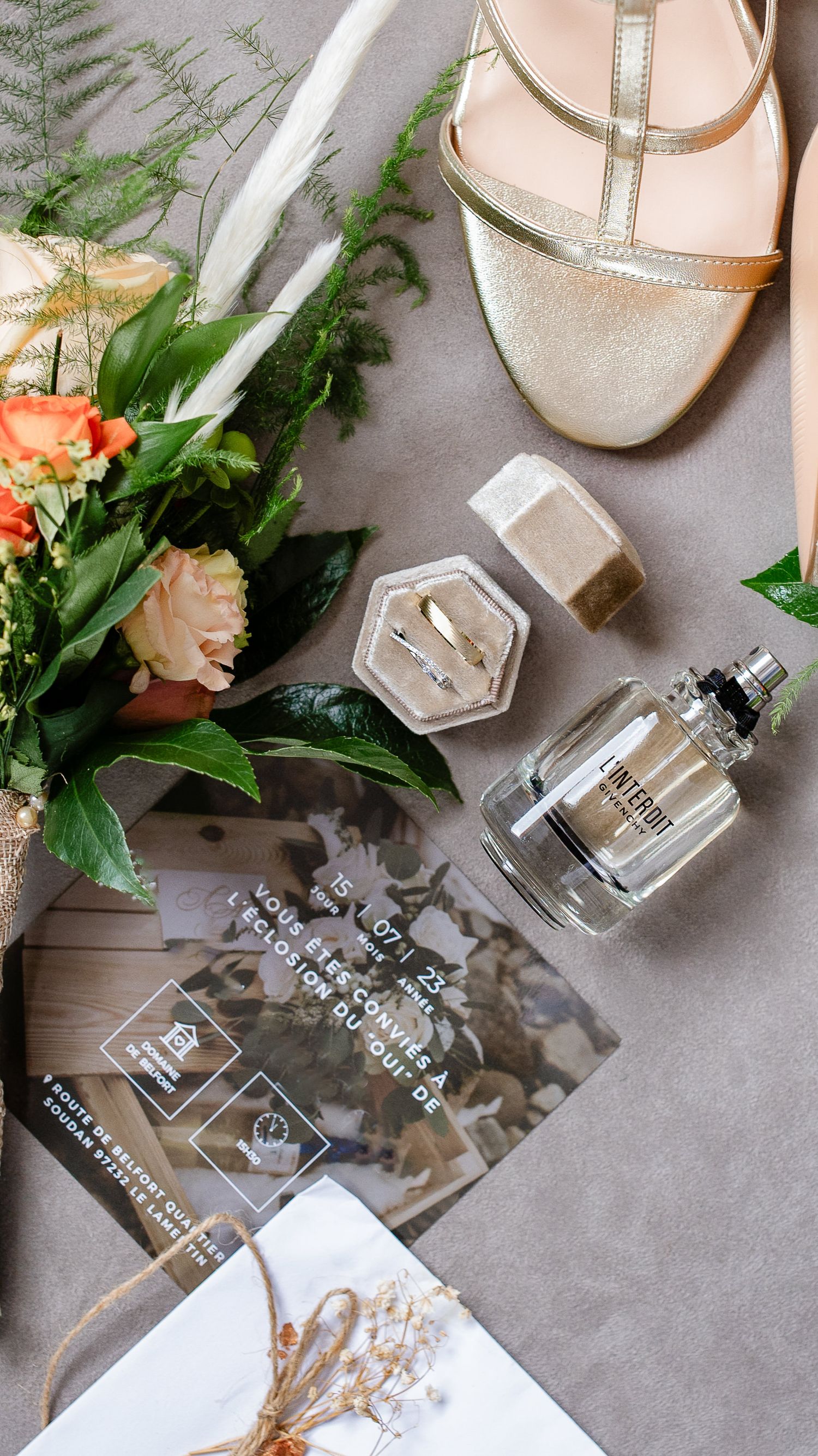 Photo en plongée des effets de la mariée, eau de toilette, alliances, chaussures et bouquet de fleurs.