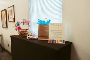 An office desk workspace with window blinds, wall decor and paper documents spread across a wooden surface.
