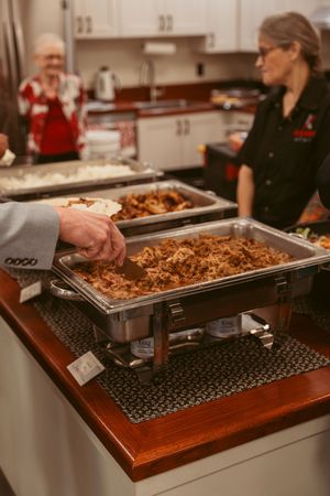 Food service buffet setup showing metal chafing dishes on wooden warming station with black grates.