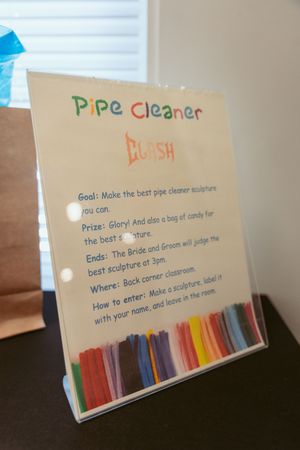 Colorful hand-written sign describing rules for a pipe cleaner craft activity displayed in a clear plastic holder.