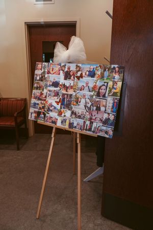 A photo display board on a wooden easel with multiple personal snapshots arranged in a collage, topped with white tulle bows.