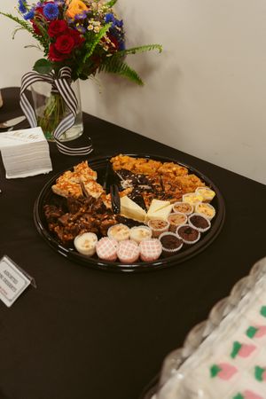 A catering platter with various appetizers and sauces sits beside a colorful floral arrangement with a striped ribbon.