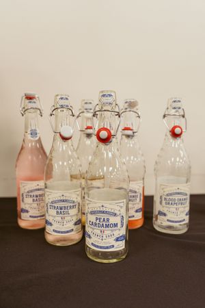 Collection of vintage-style glass bottles with wire bail tops containing various flavored drinks and syrups.
