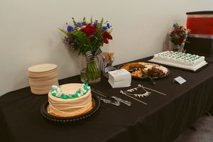 An elegant cake table display features seven white-frosted cakes of different sizes arranged on black tablecloths.