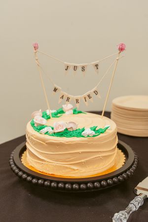 A vanilla frosted layer cake on a black platter decorated with green frosting accents and a delicate string bunting banner.