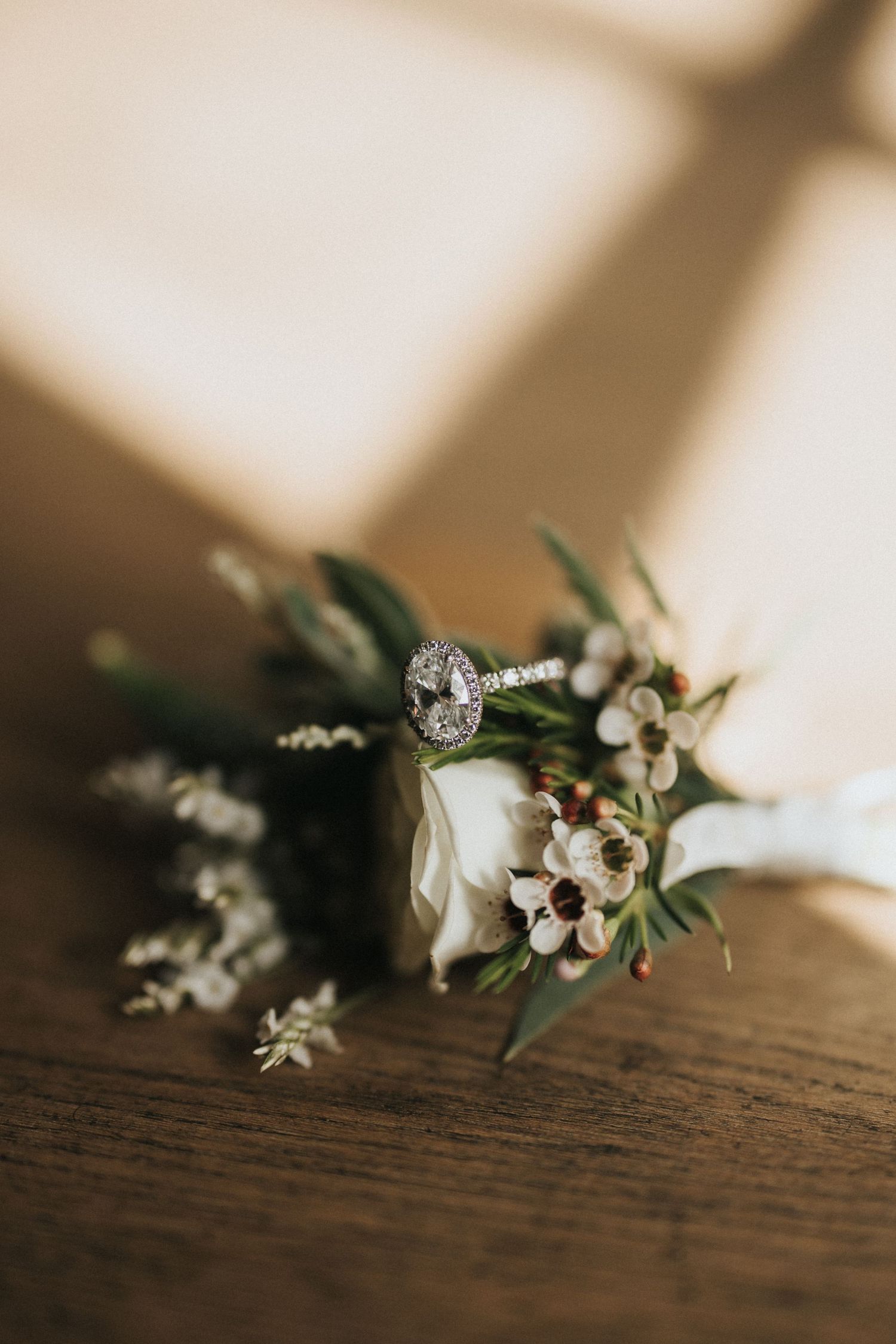 Small white flowers and delicate blossoms with green foliage arranged on a dark wooden surface in warm lighting.
