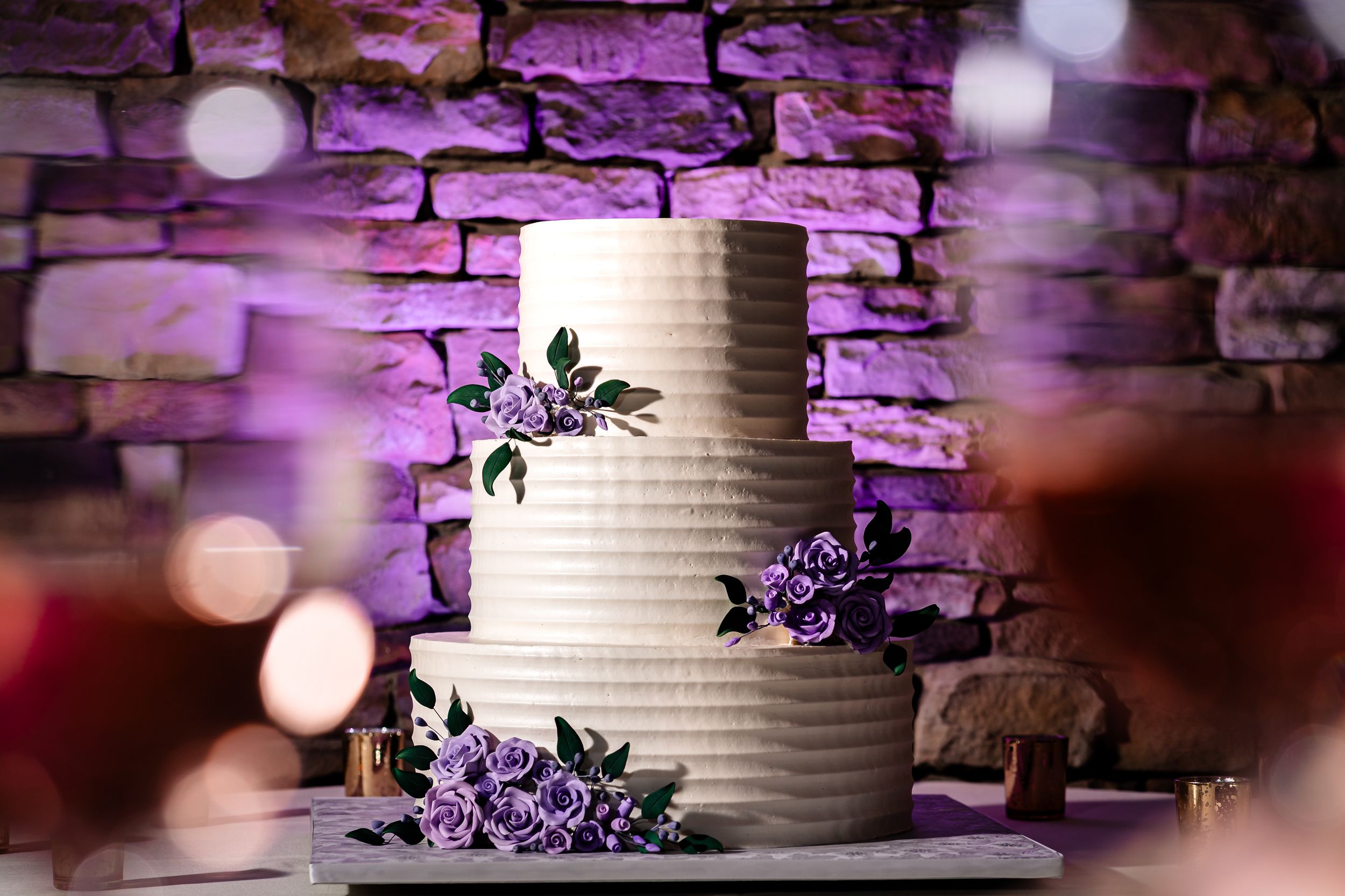 Purple uplighting illuminates a textured stone wall with decorative elements.