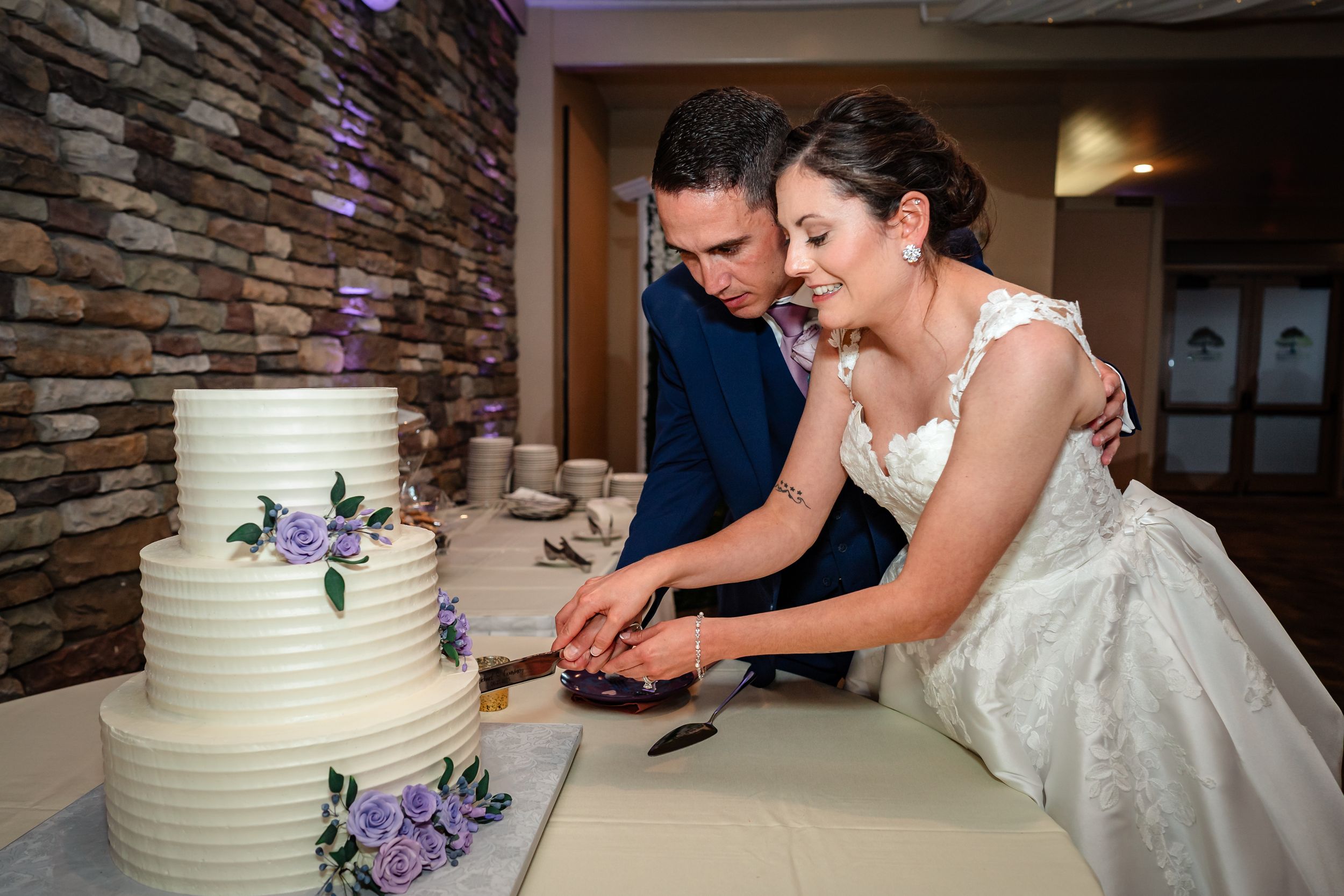 Couple cutting their white tiered wedding cake together at the reception.