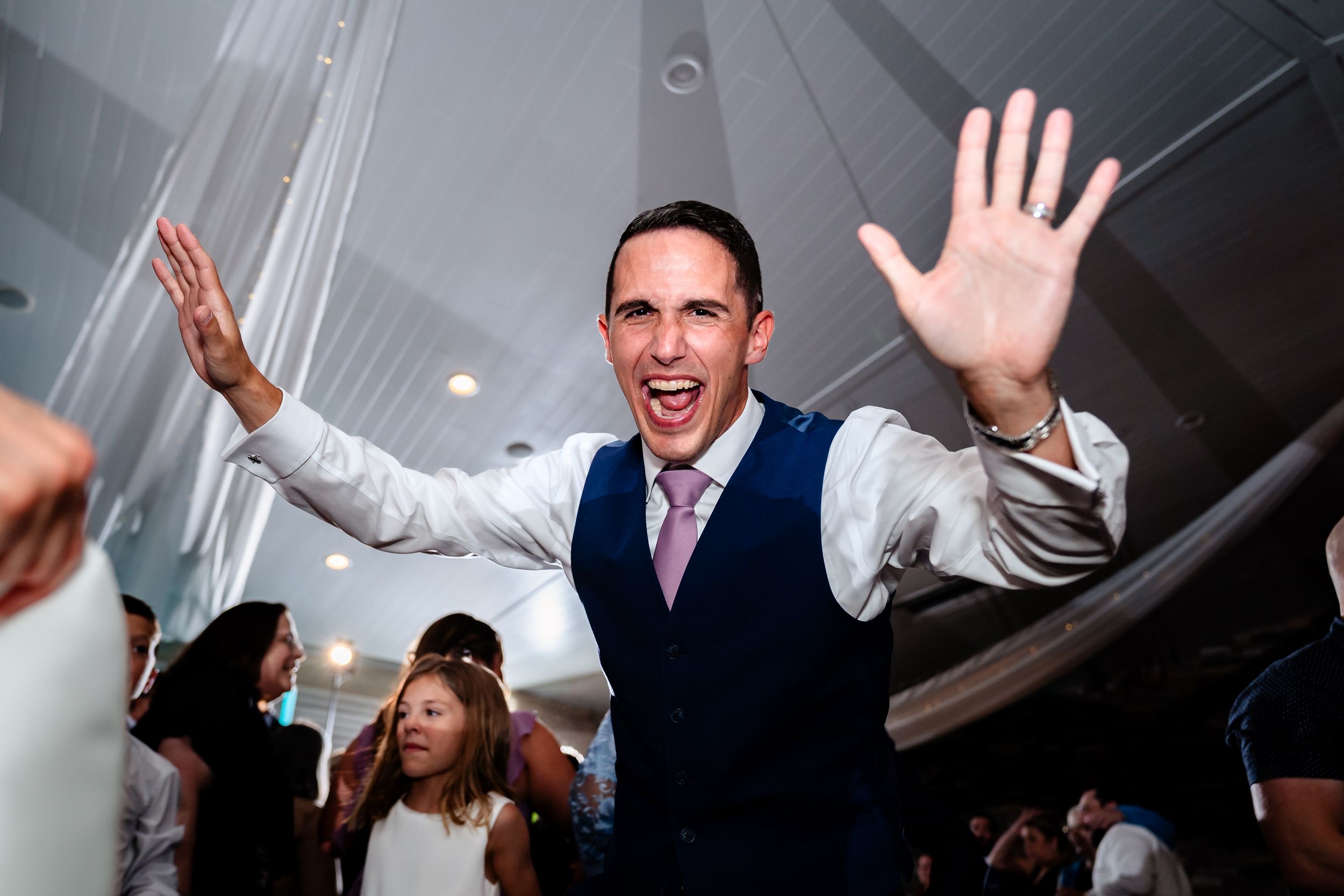 Wedding guests dancing and celebrating on a crowded dance floor with raised hands and joyful expressions.