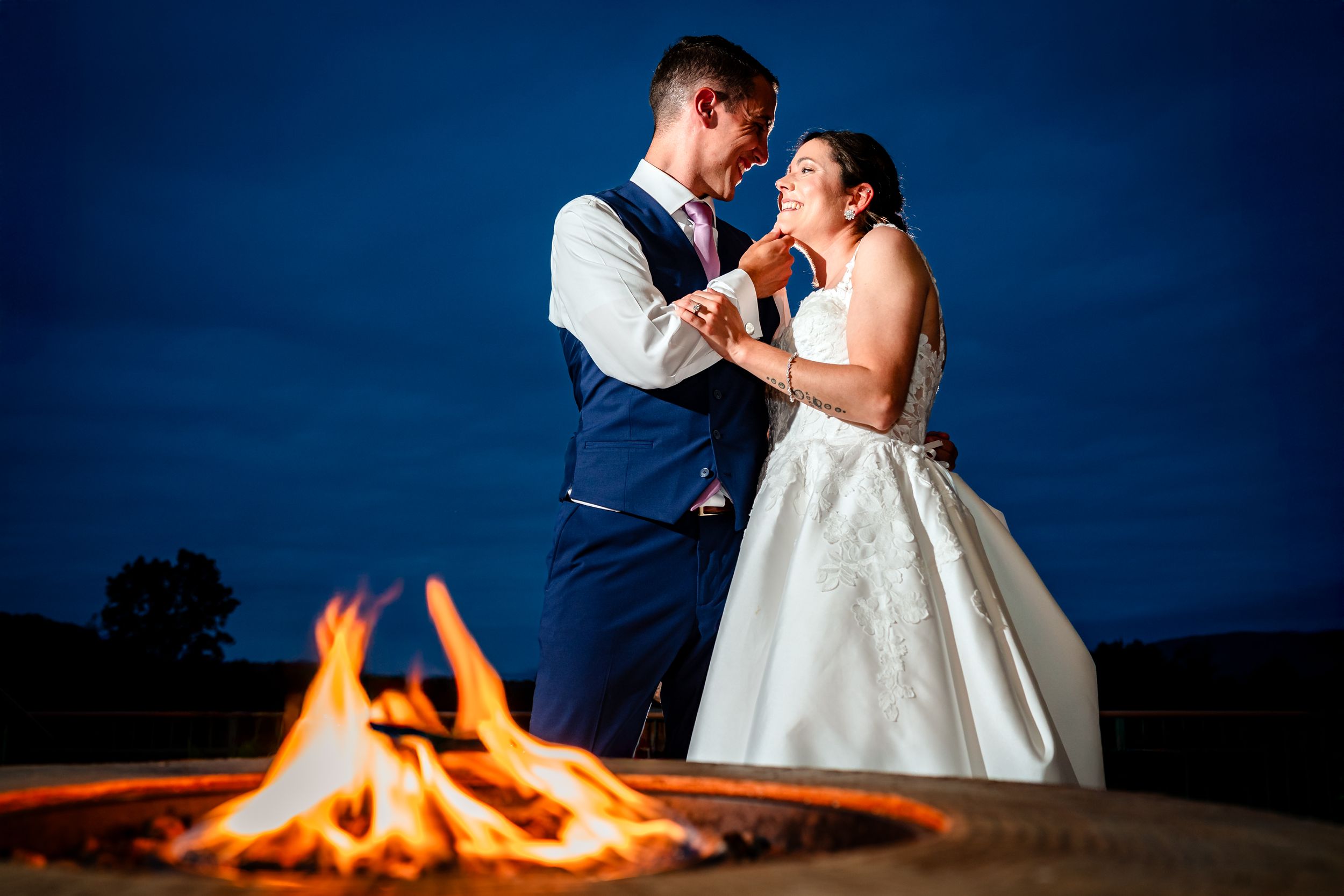 Romantic outdoor nighttime wedding scene with glowing fire pit in the background.