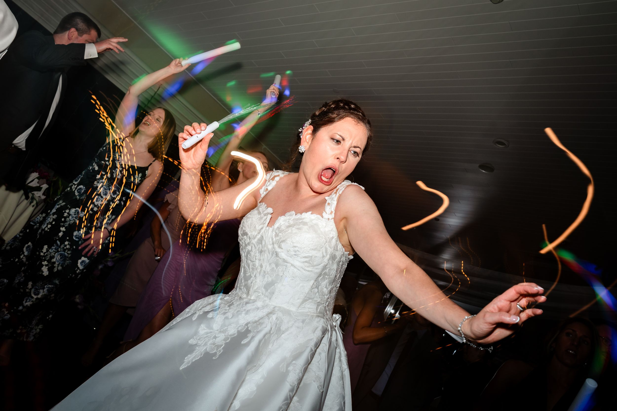 Wedding party dancing with green and blue LED light sticks creating light trails in the dark.