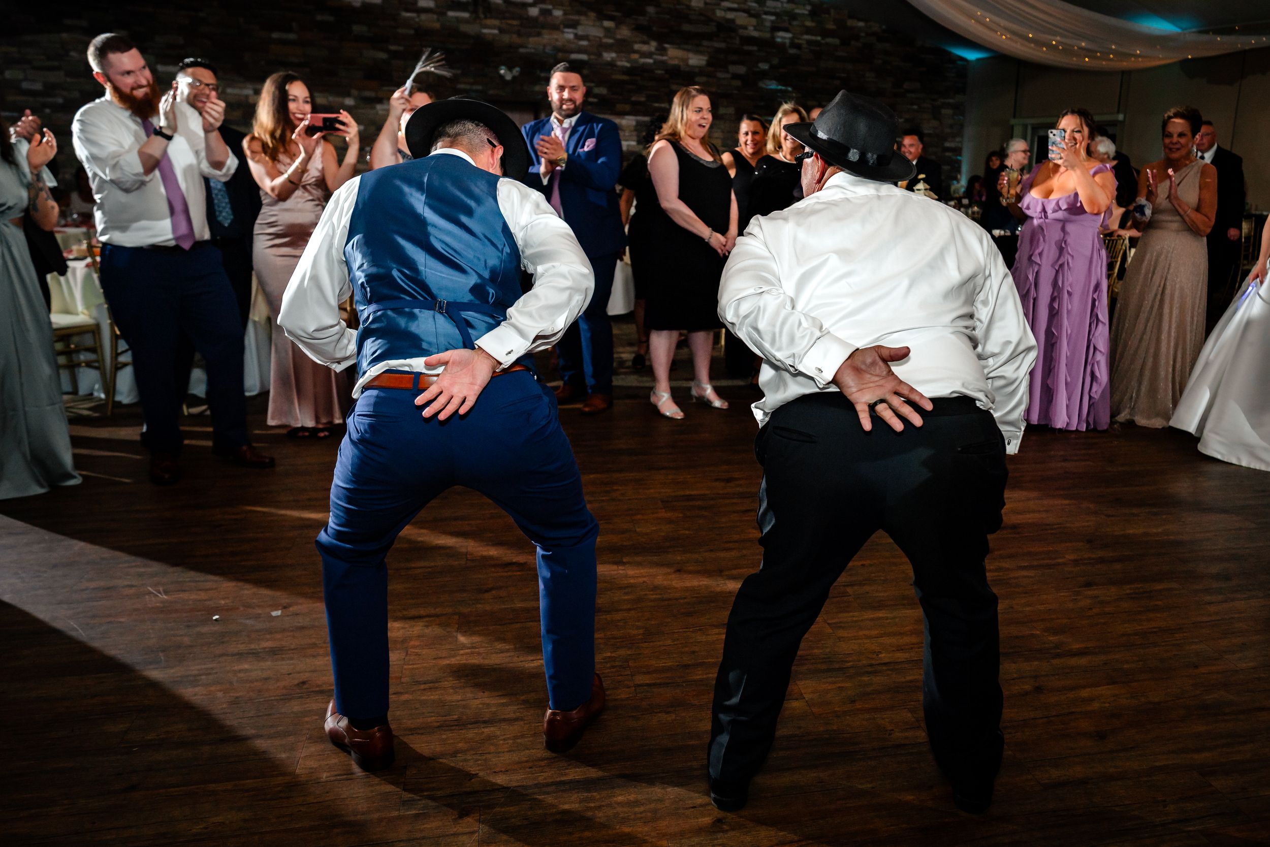 Wedding guests performing synchronized dance moves on a wooden dance floor.