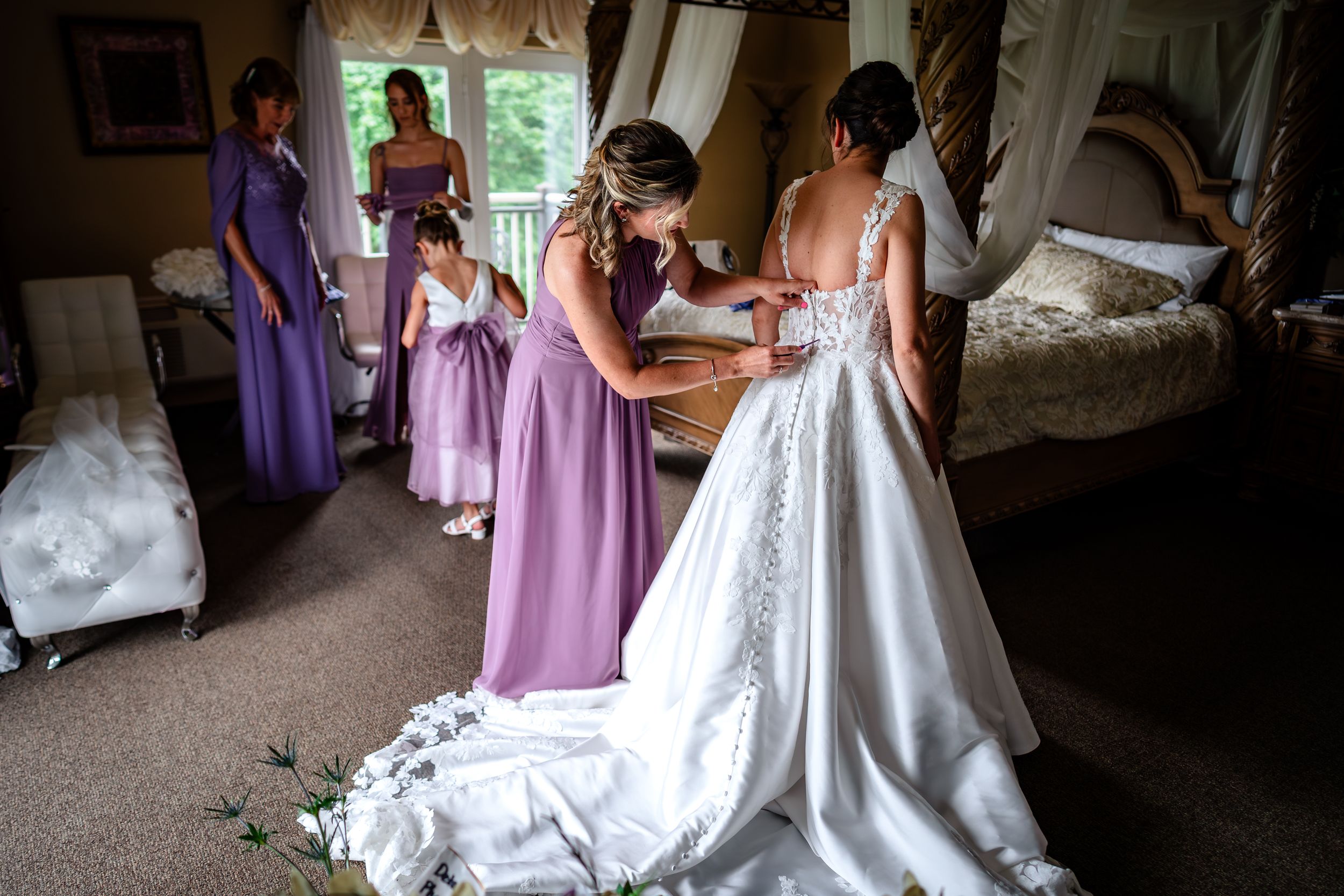 Wedding dress being adjusted with bridesmaids in purple dresses helping.