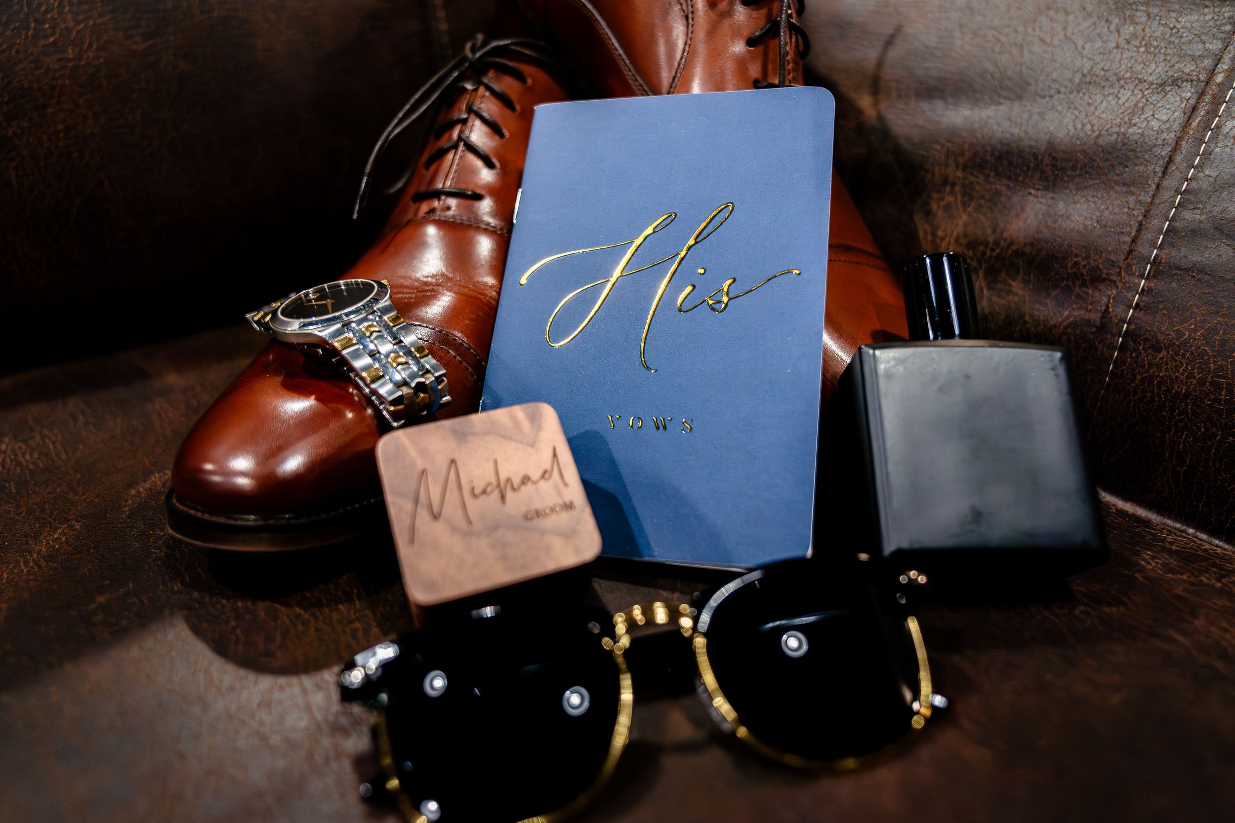 Wedding details including brown leather shoes and blue stationery on dark surface.