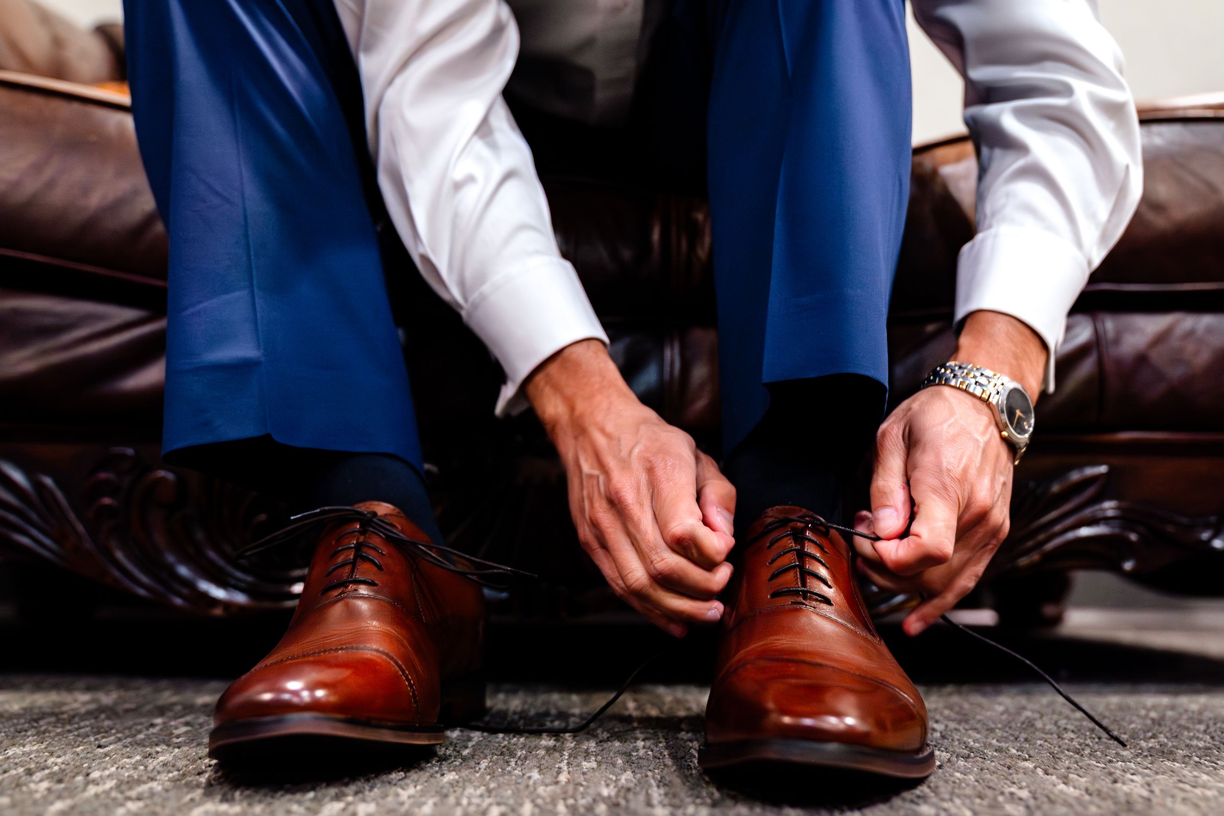 Close-up of brown leather dress shoes being put on with navy blue suit pants.
