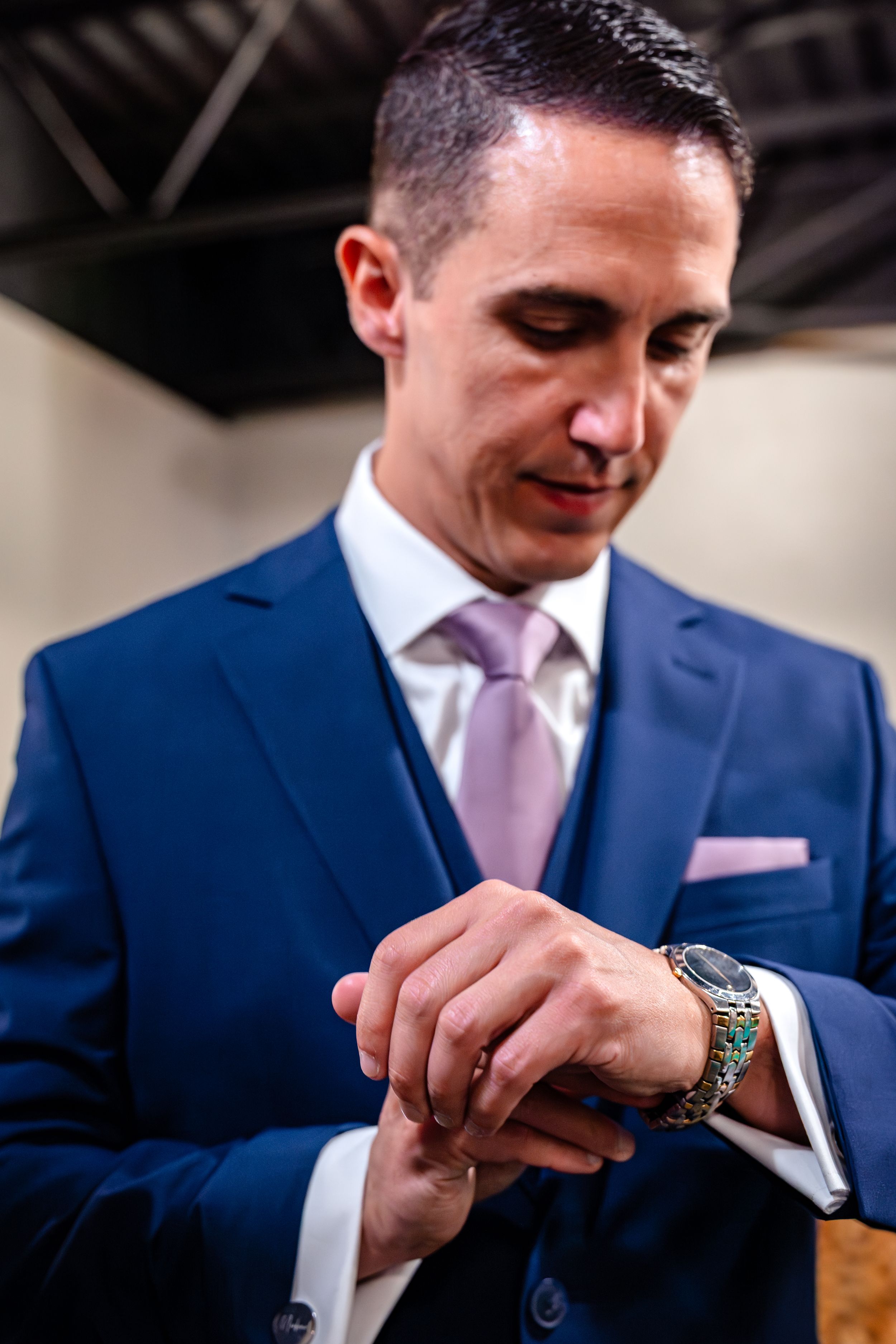 Close-up of wristwatch and cufflinks with navy suit and pink tie details.