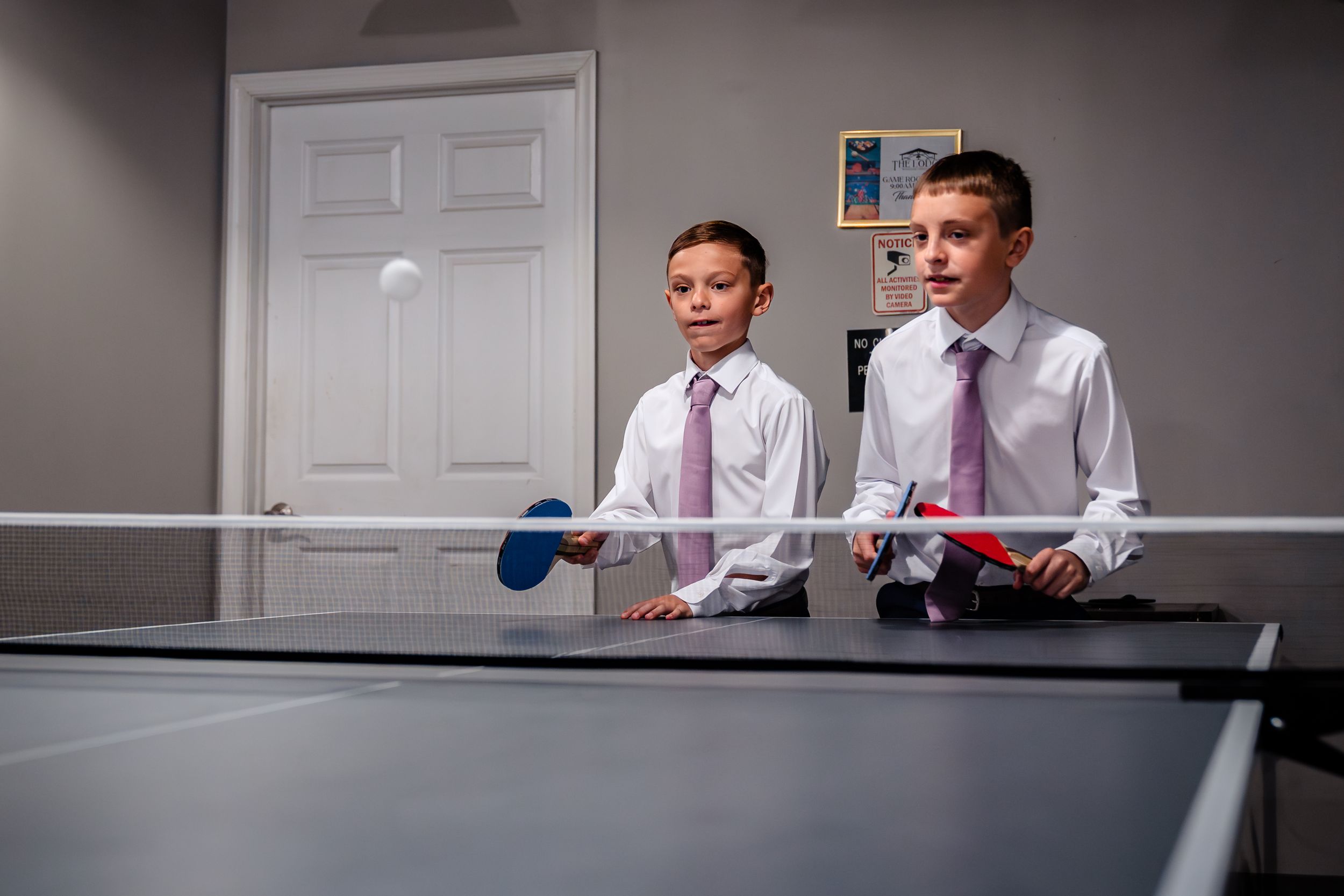 Wedding party members playing ping pong in formal attire.