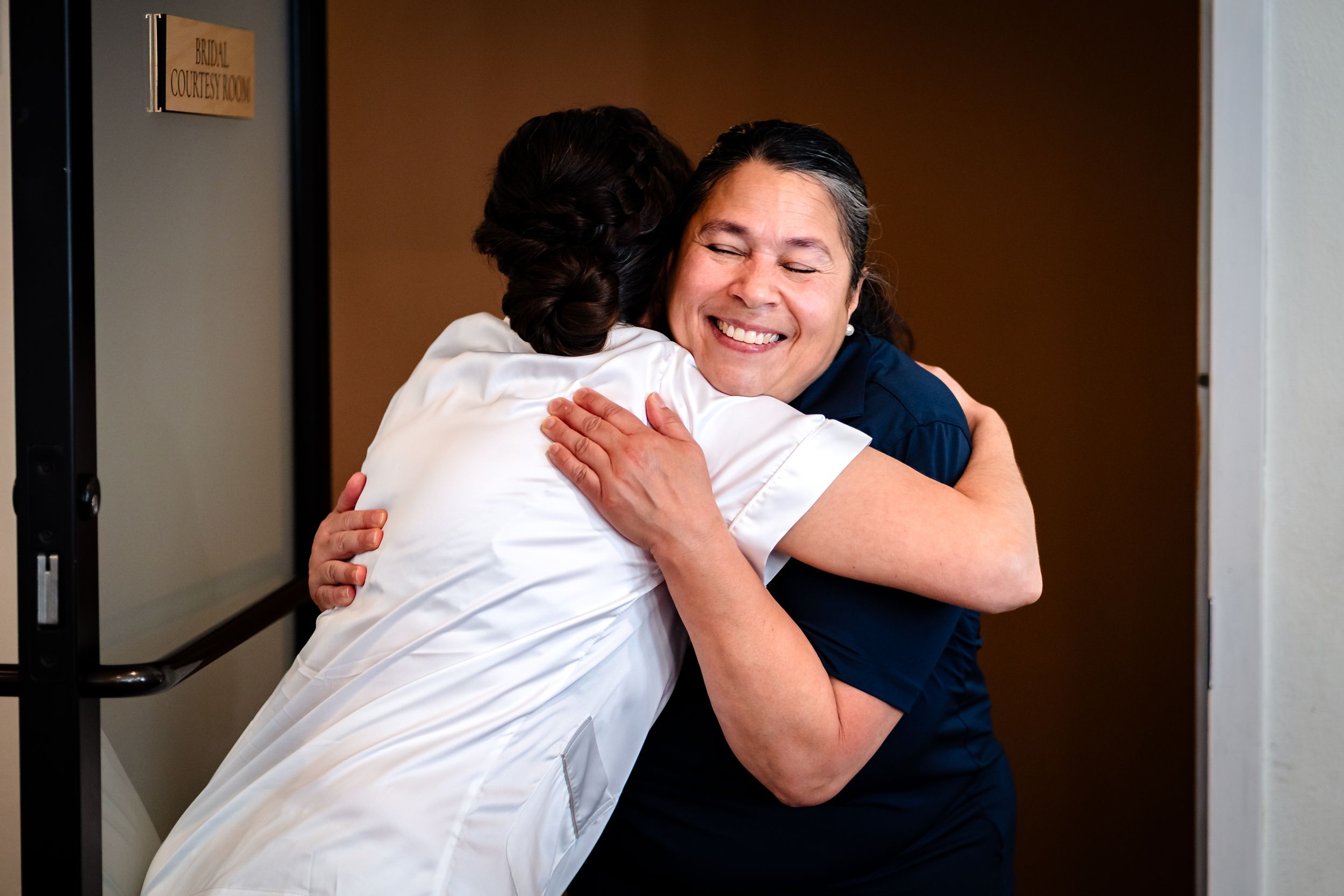 Warm hugs and laughter shared between wedding party members in a dimly lit room.