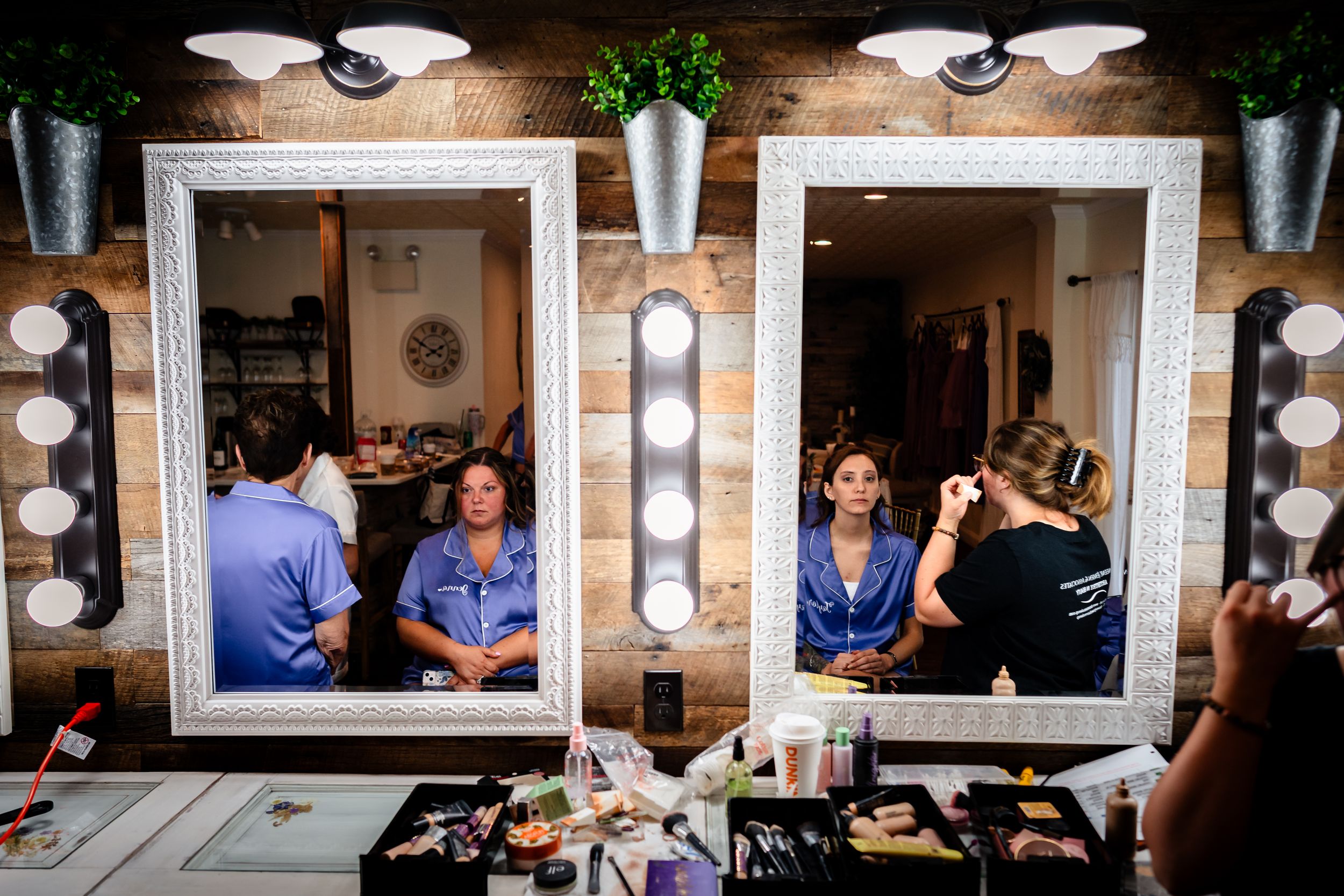 Row of illuminated makeup mirrors in a dressing room with people getting ready.