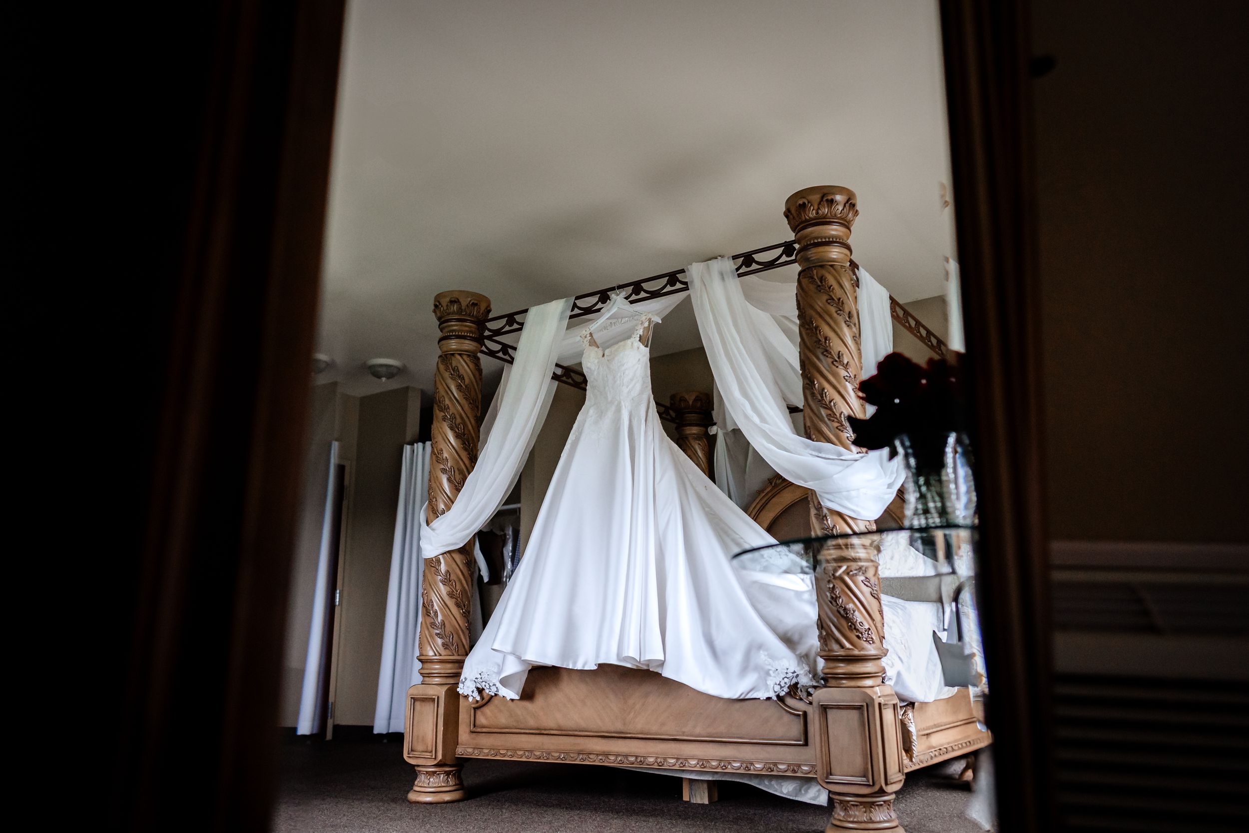 White wedding dress hanging in window light creating dramatic silhouette.