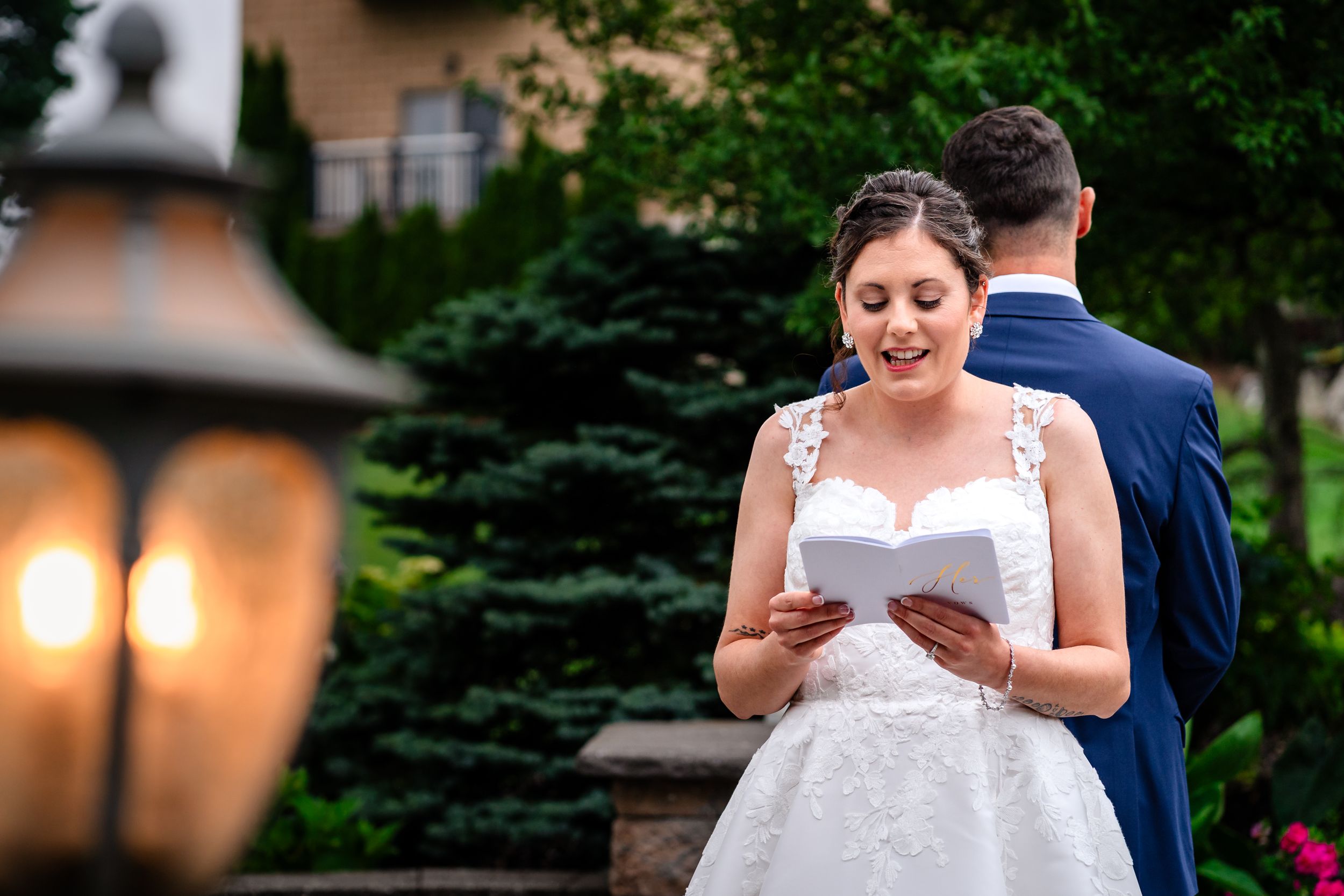 Couple reading personal vows during an outdoor wedding ceremony with green foliage in the background.