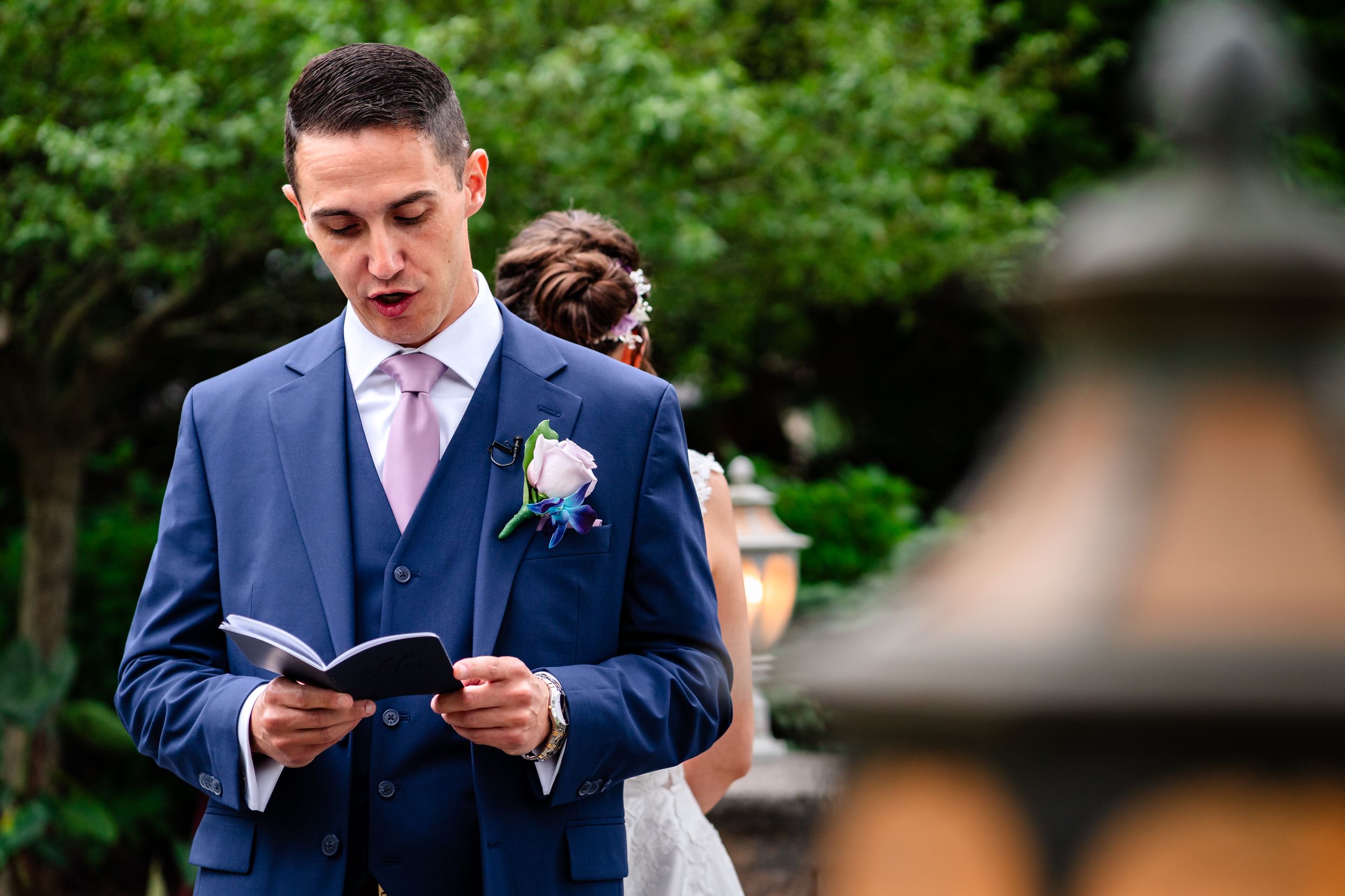 Wedding couple exchanging vows in a garden setting with lanterns and evergreen trees.