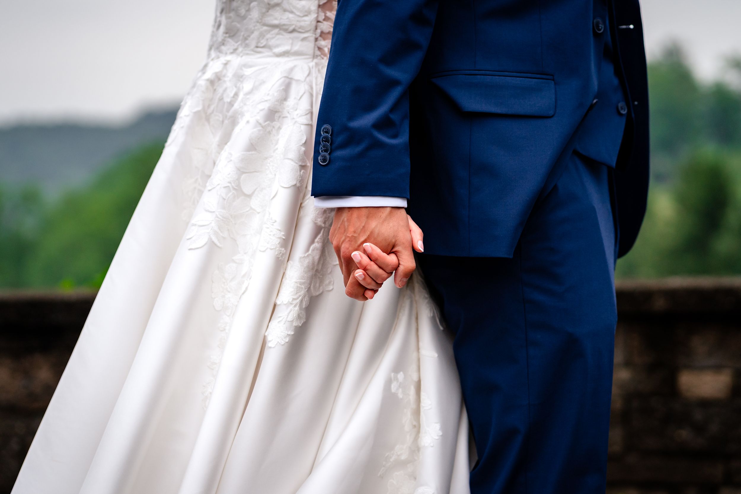 Bride and groom in navy suit standing together during outdoor ceremony against scenic landscape.