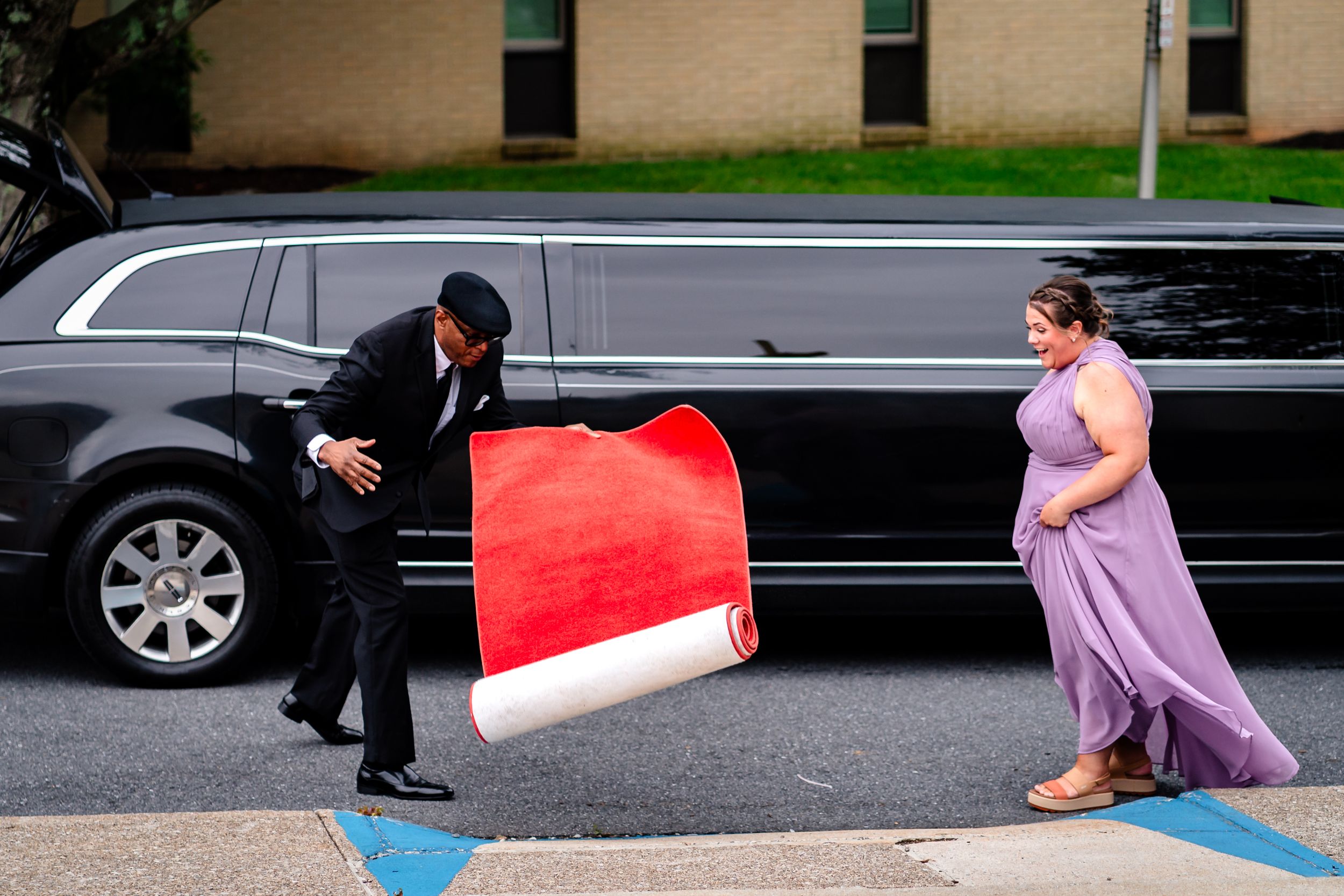Wedding party members helping with dress arrangements in a parking lot.