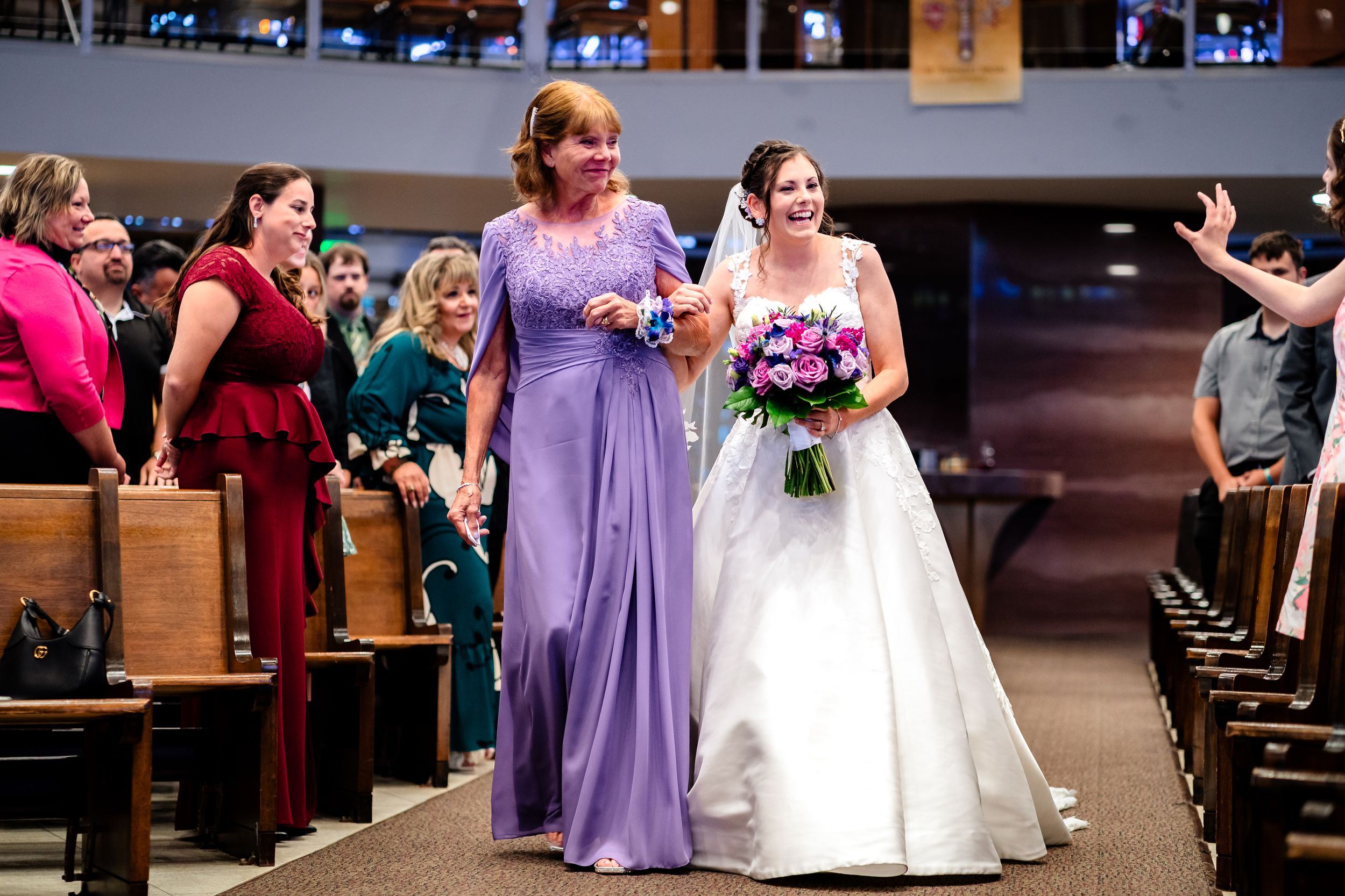 Wedding party in purple dresses and white gown walking down church aisle.