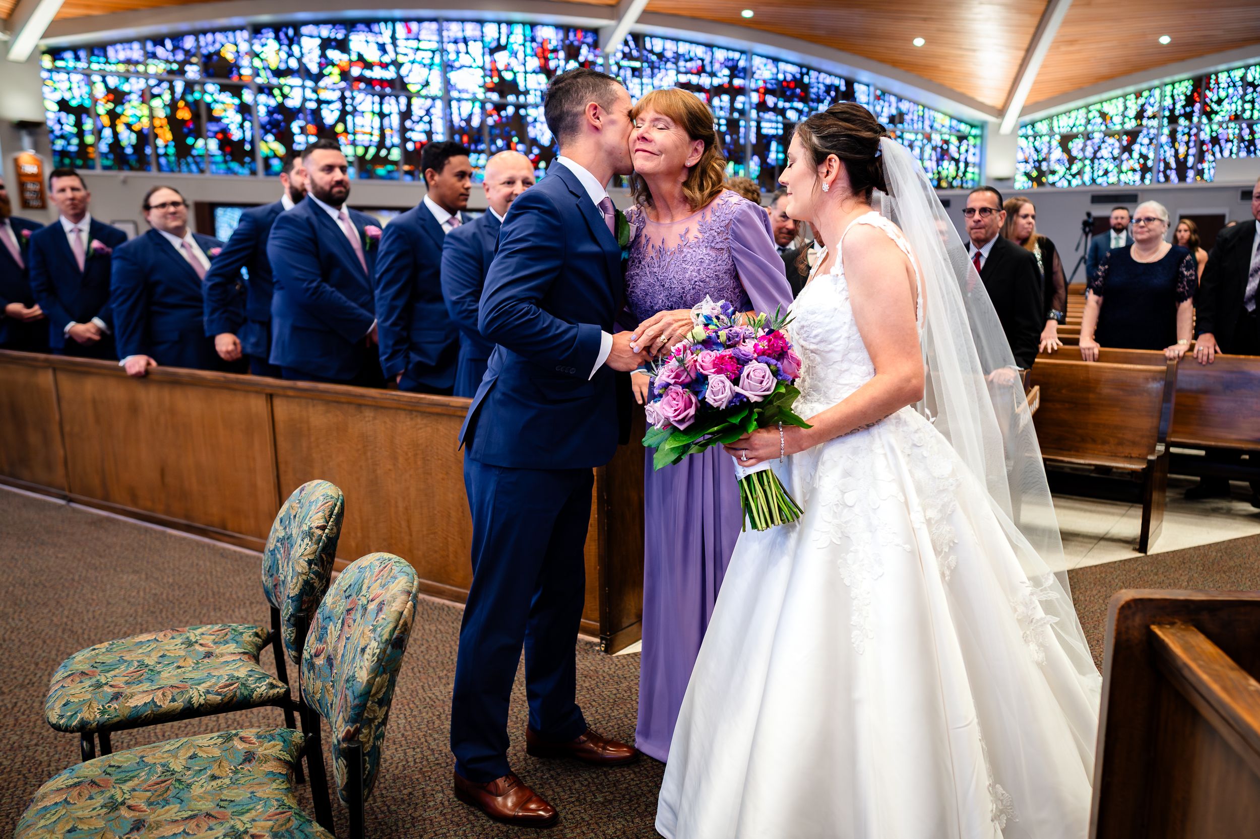 Wedding ceremony in a church with bridesmaids in purple dresses holding vibrant floral bouquets.