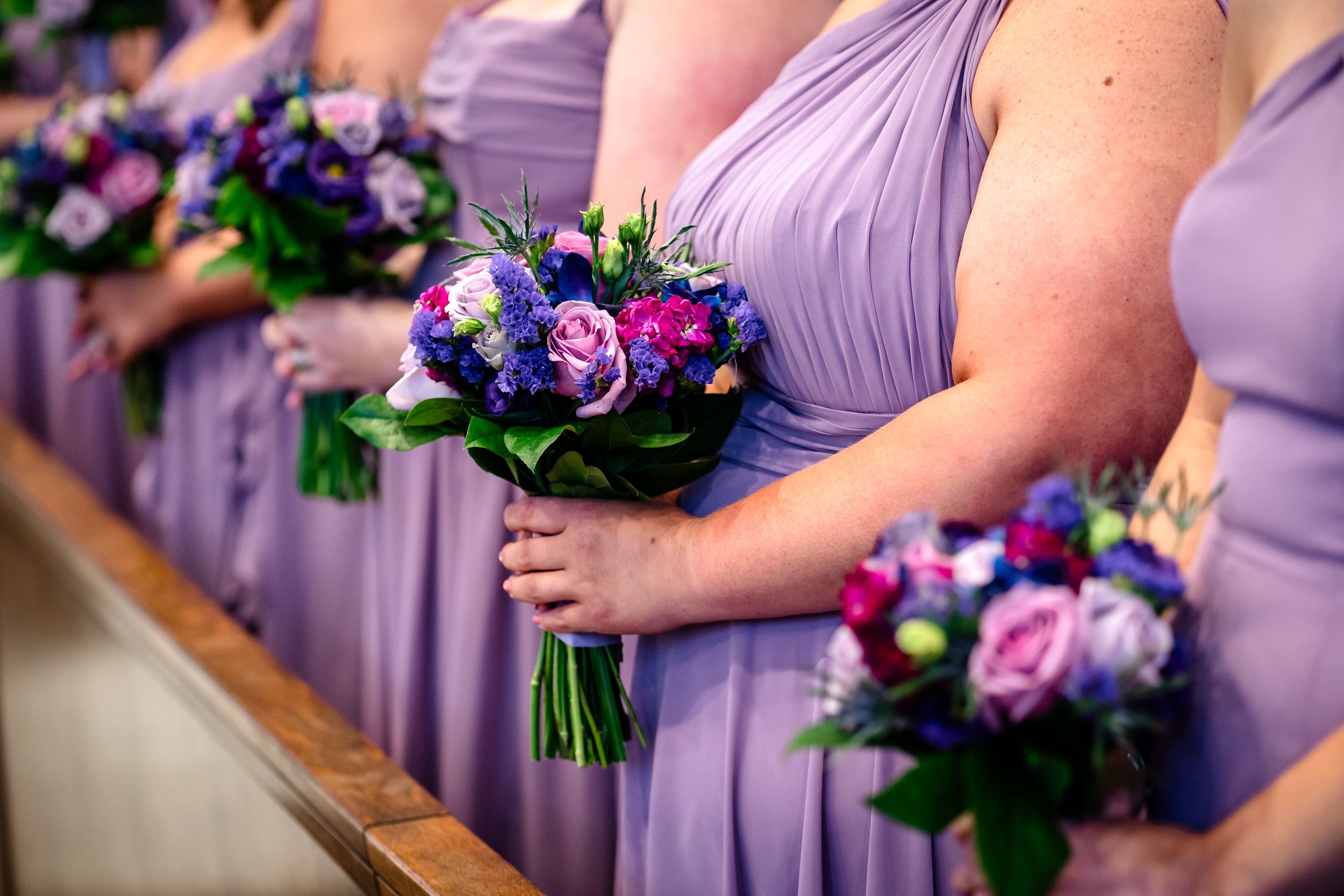 Close-up of bridesmaids holding purple and pink bouquets while wearing lavender dresses.