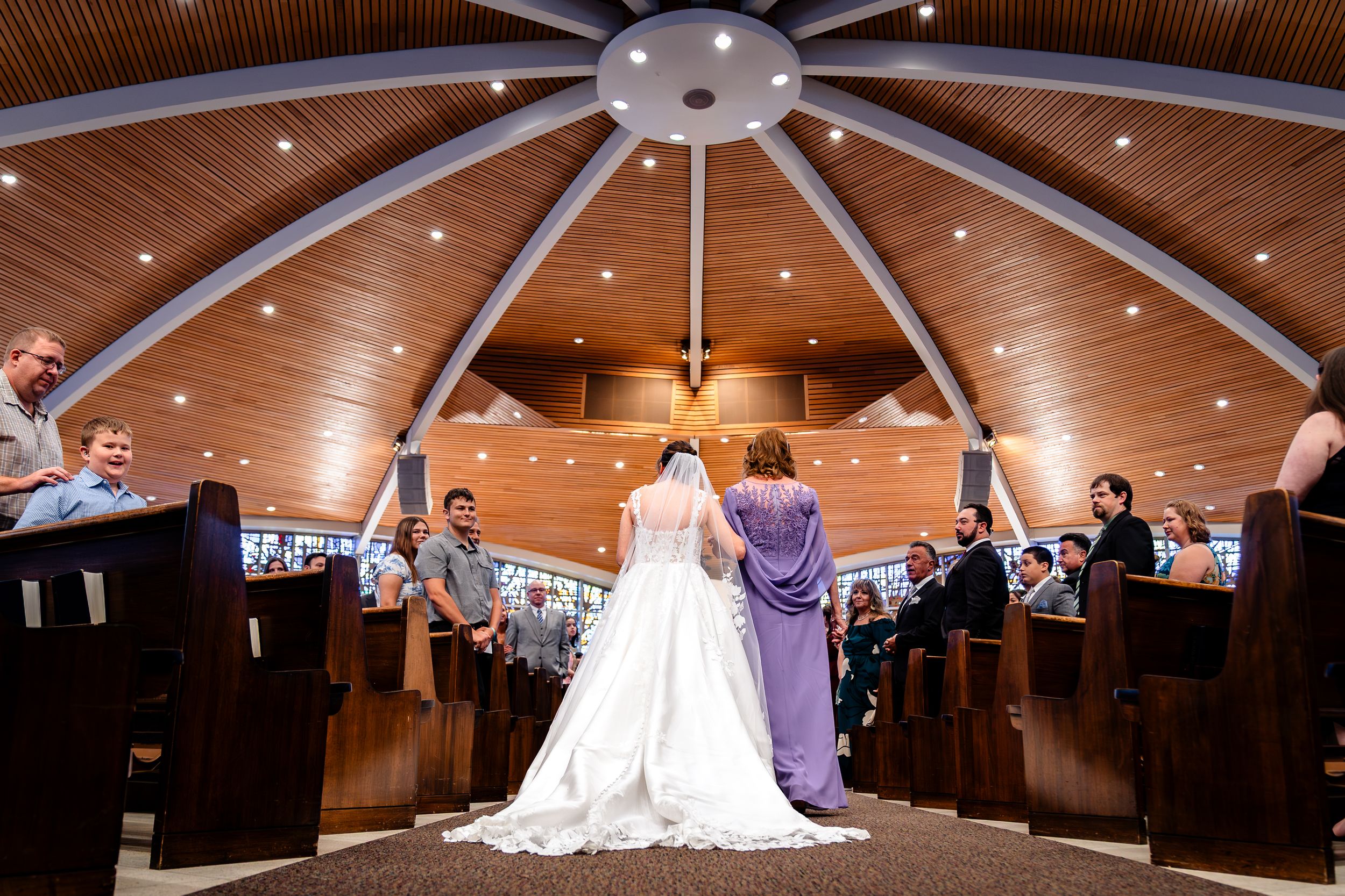 Wedding ceremony under a dramatic wooden domed ceiling with radial beams in a modern church.