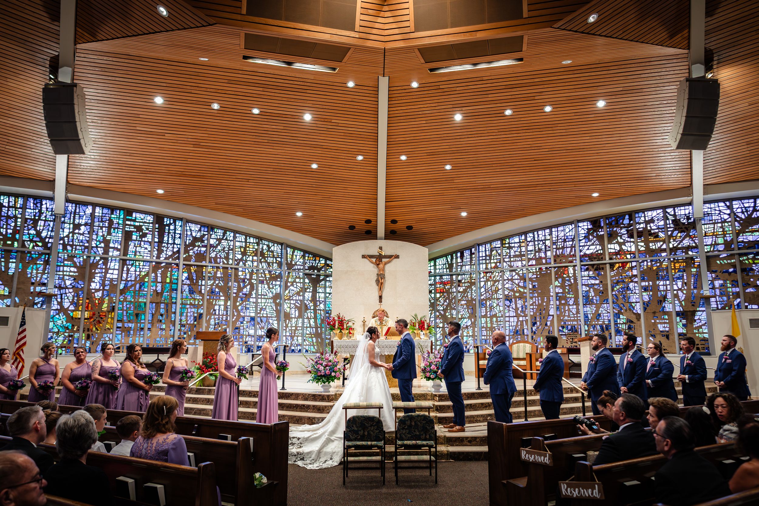 Wedding ceremony in modern church with dramatic stained glass windows and wooden architectural details.
