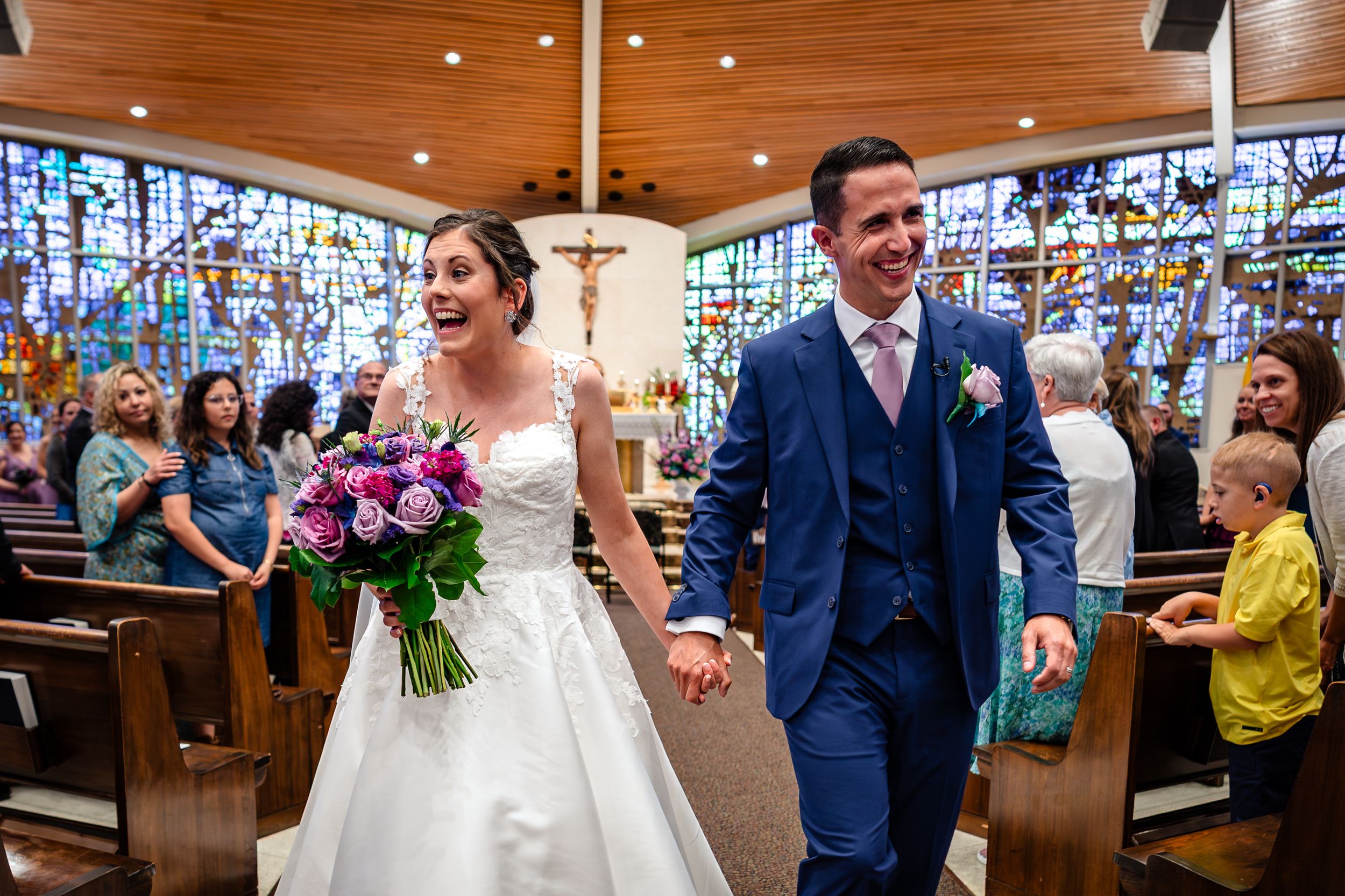 Wedding celebration inside a church with wooden ceiling and colorful stained glass windows.