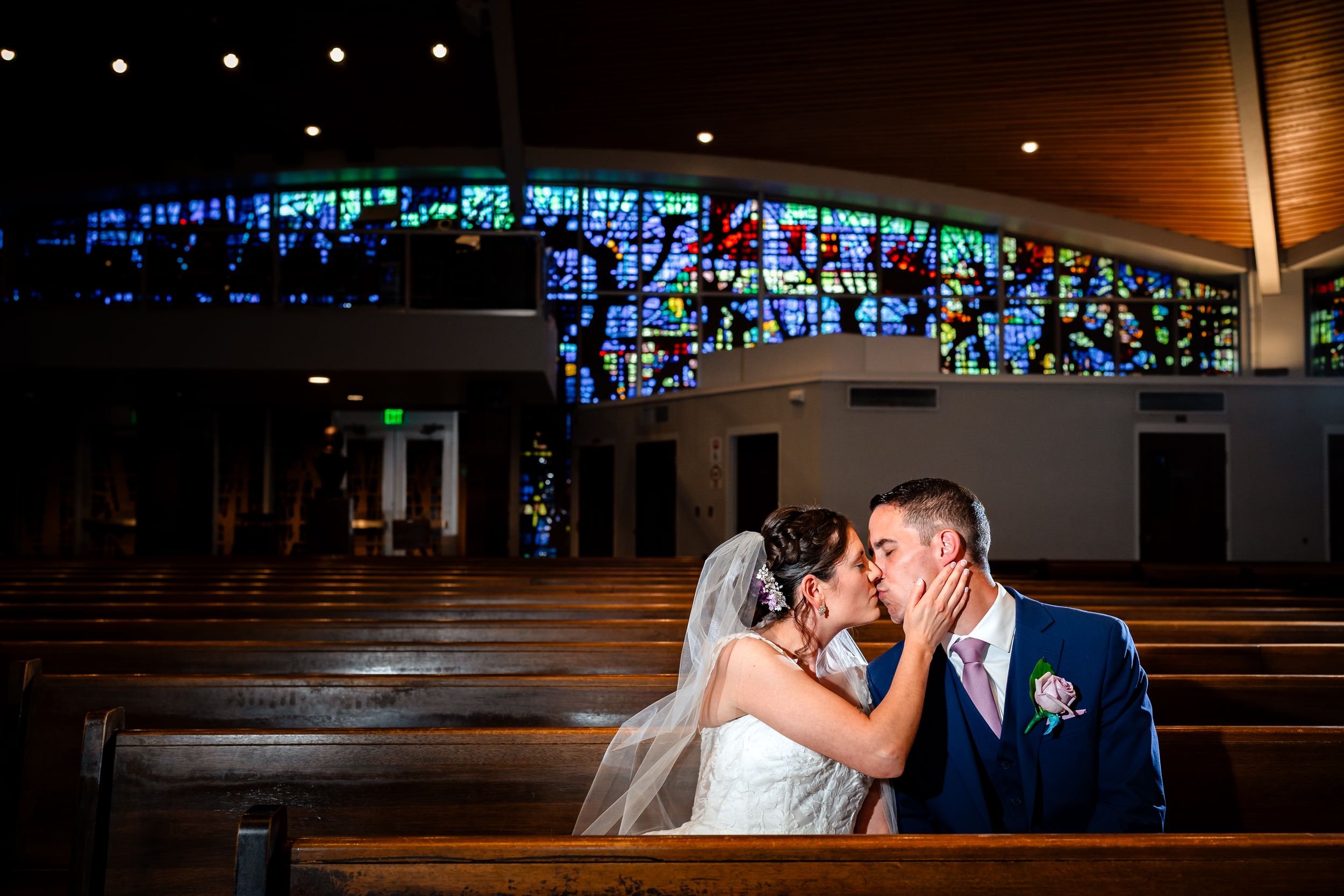 Romantic wedding ceremony moment captured in church with dramatic lighting and stained glass backdrop.