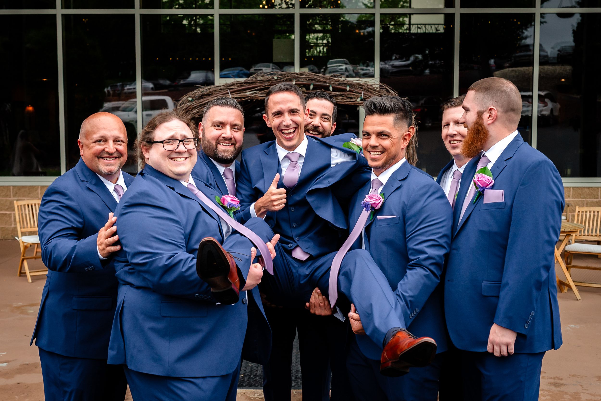 Groomsmen in navy suits pose playfully outside wedding venue.