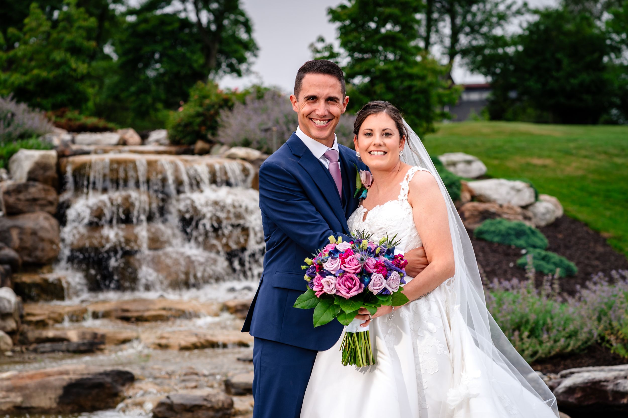 Scenic outdoor wedding photos with cascading waterfall feature and landscaped grounds.