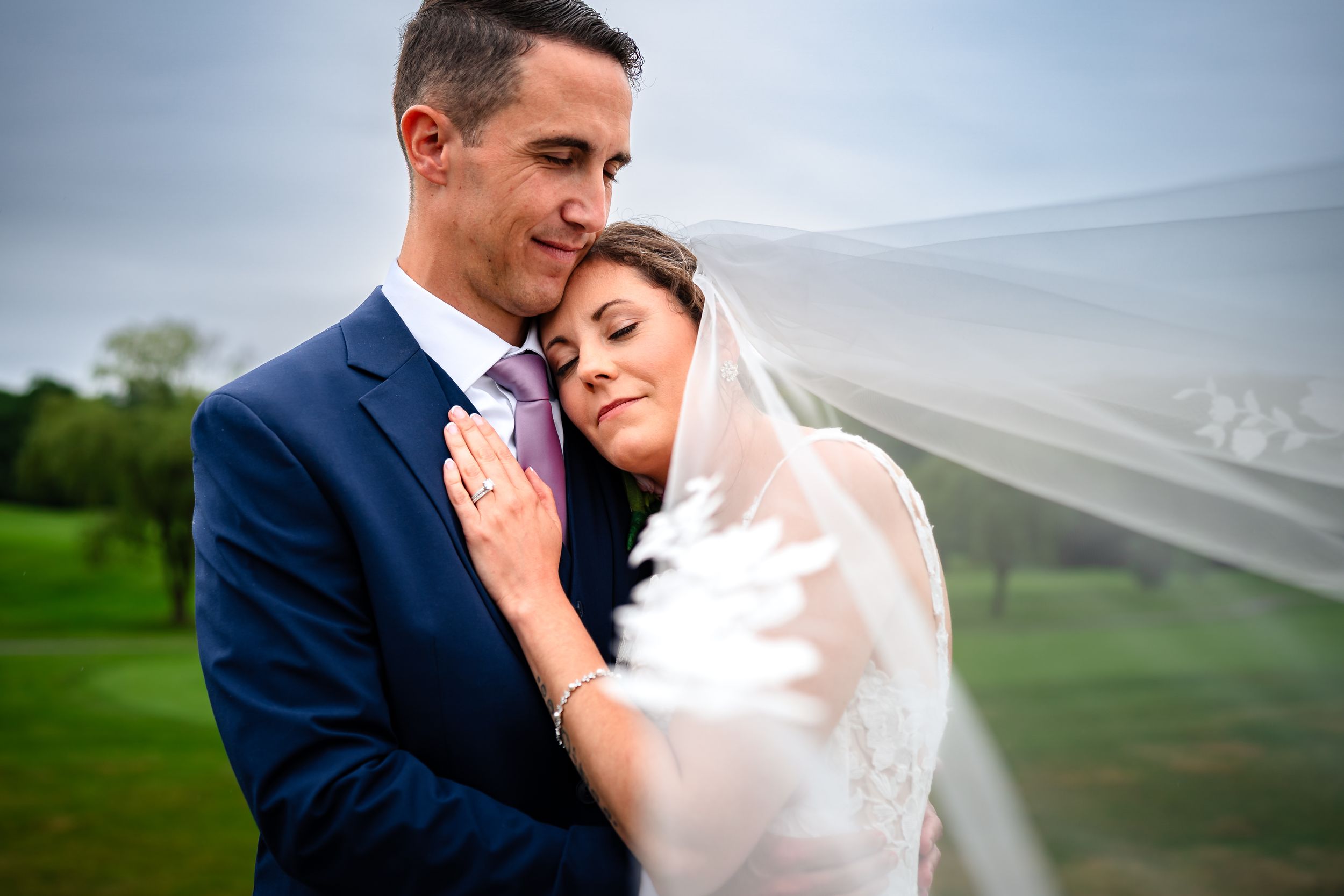 Intimate wedding portrait of couple embracing outdoors on a green hillside.