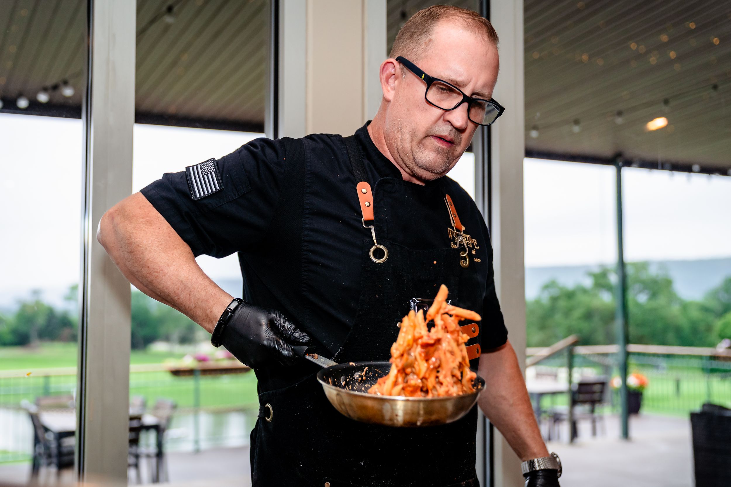 Chef in black uniform preparing flaming dish at outdoor restaurant venue.
