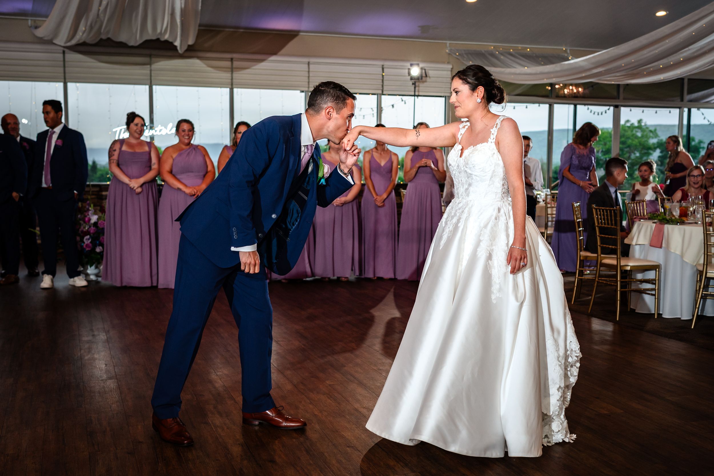 Couple performs playful first dance at wedding reception with bridesmaids in purple dresses watching.