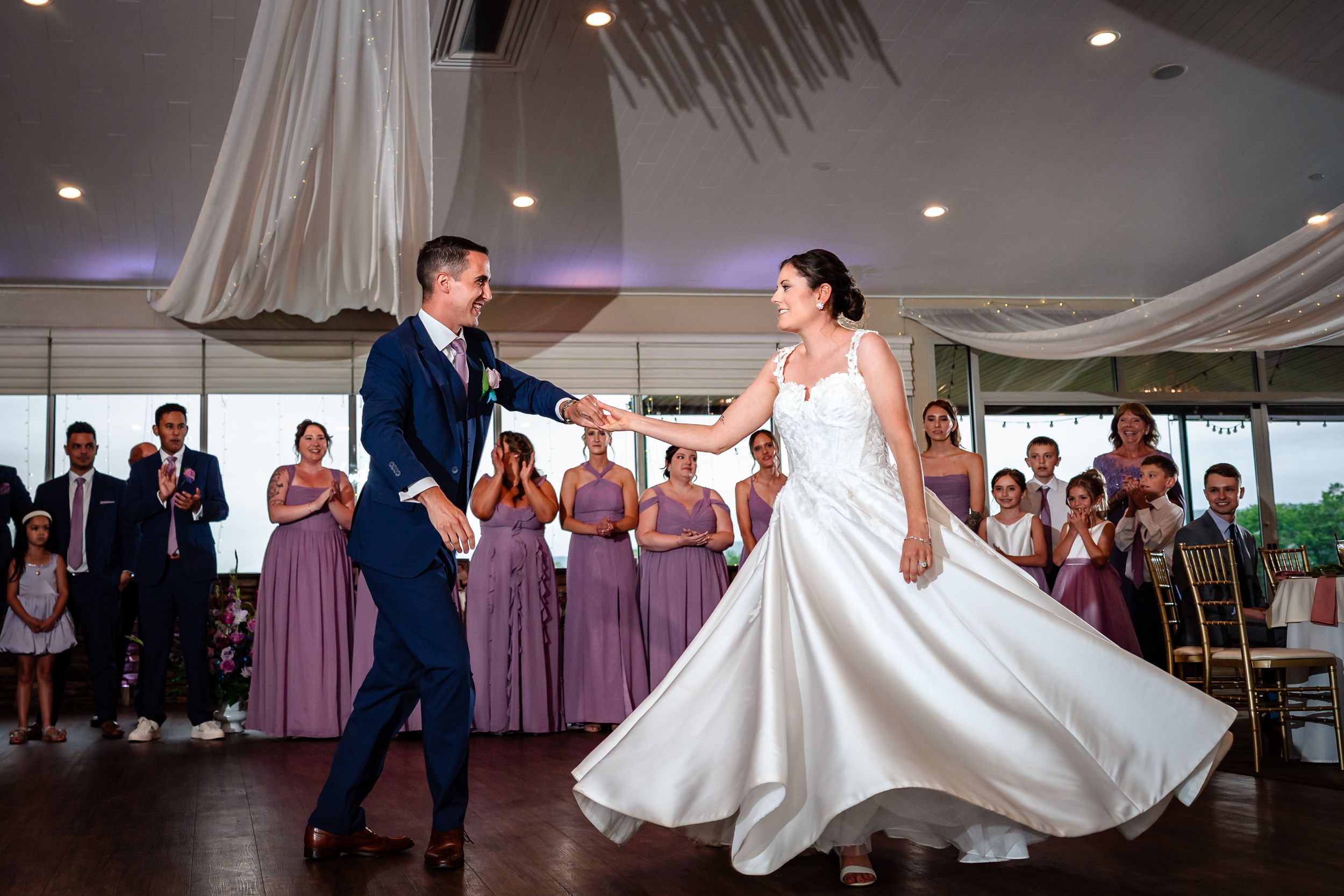 Newlyweds sharing energetic dance moment at reception with bridesmaids in background.