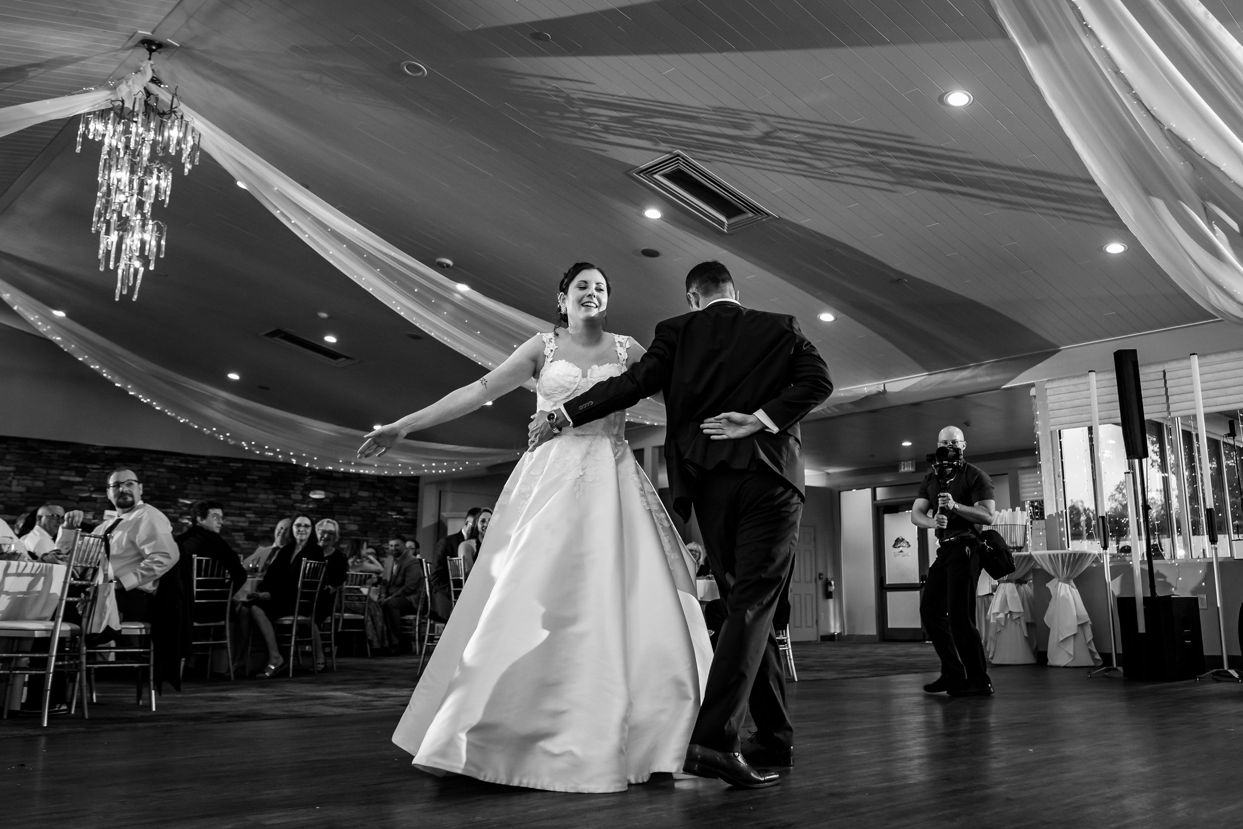 Black and white photo of couple dancing under elegant draped ceiling at wedding reception.