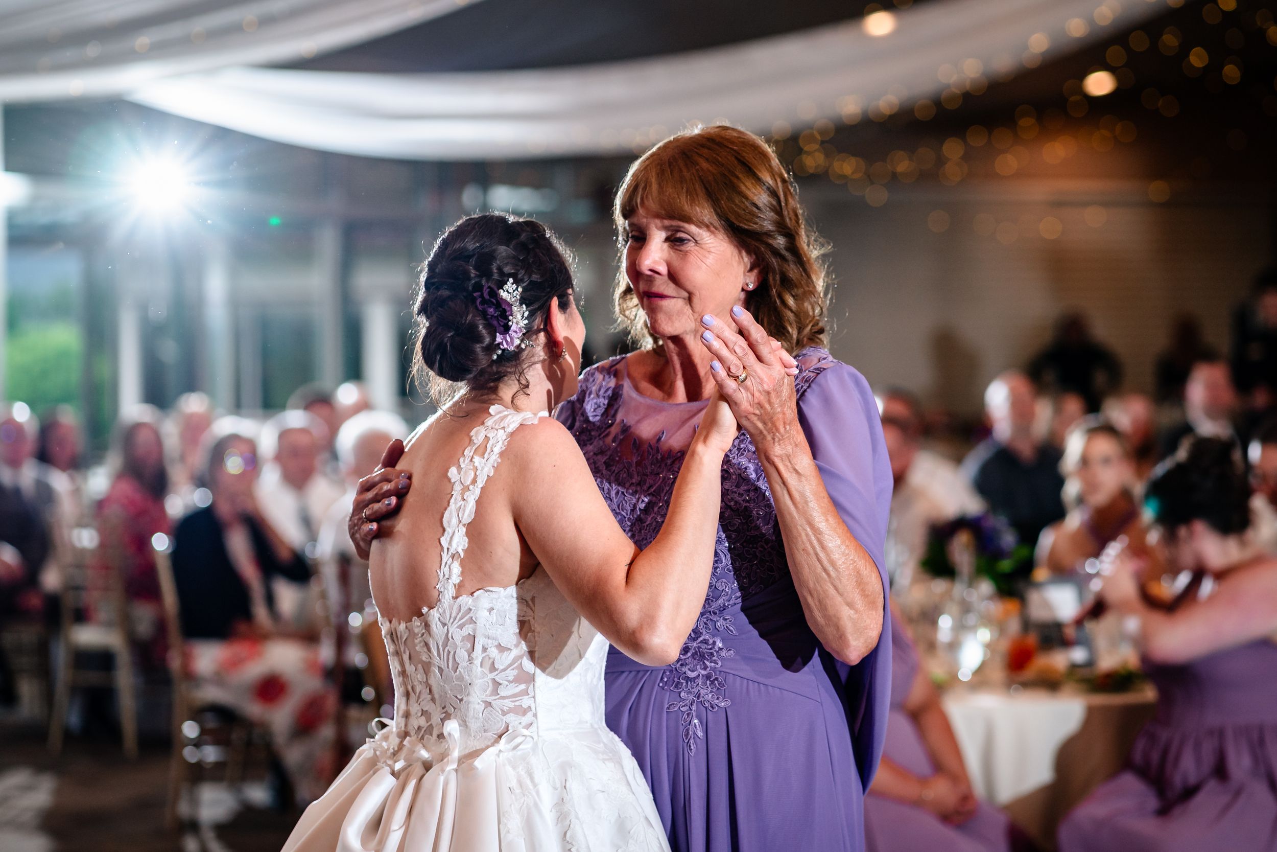 Emotional moment between bride and guest in purple dress during wedding reception.