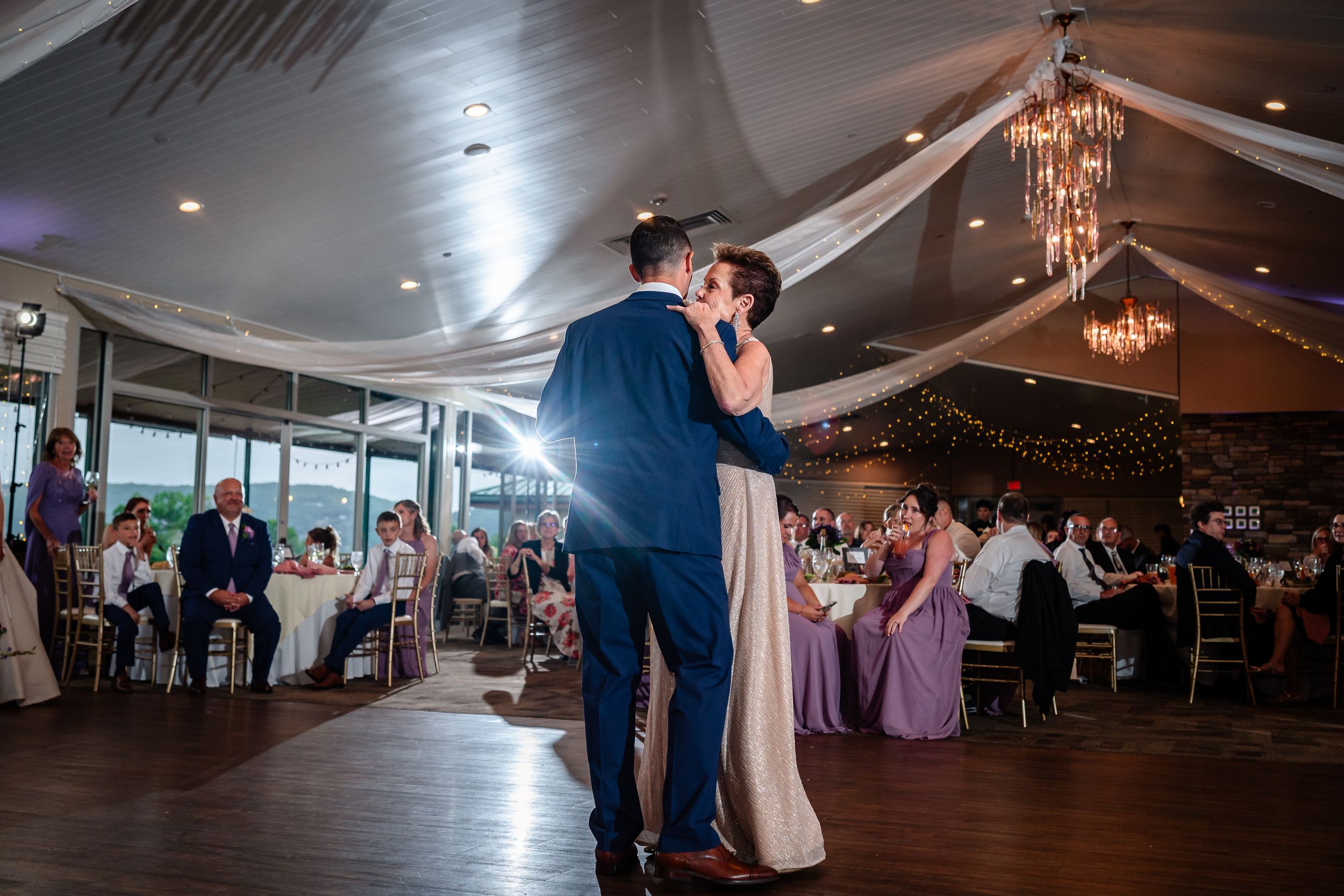 Couples dancing at an elegant wedding reception under draped fabric and chandeliers.